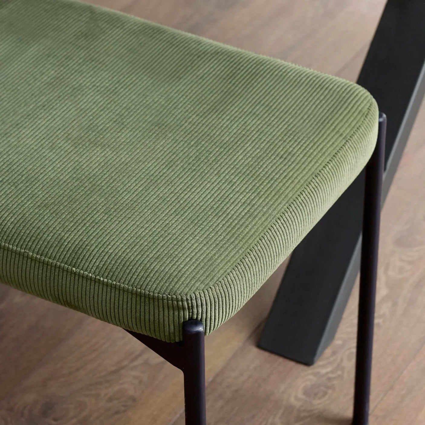 Green corduroy dining chair seat with black metal legs on wooden floor