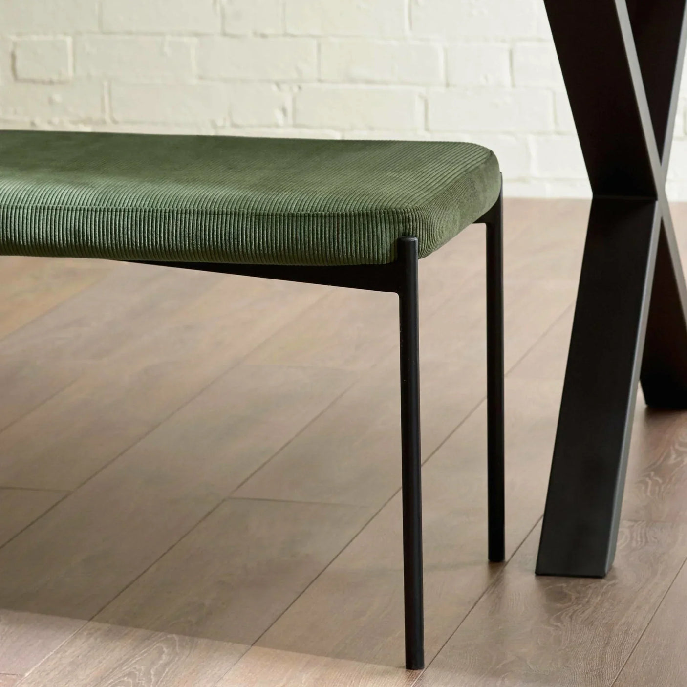 Green upholstered dining bench with slim black legs on light wood floor