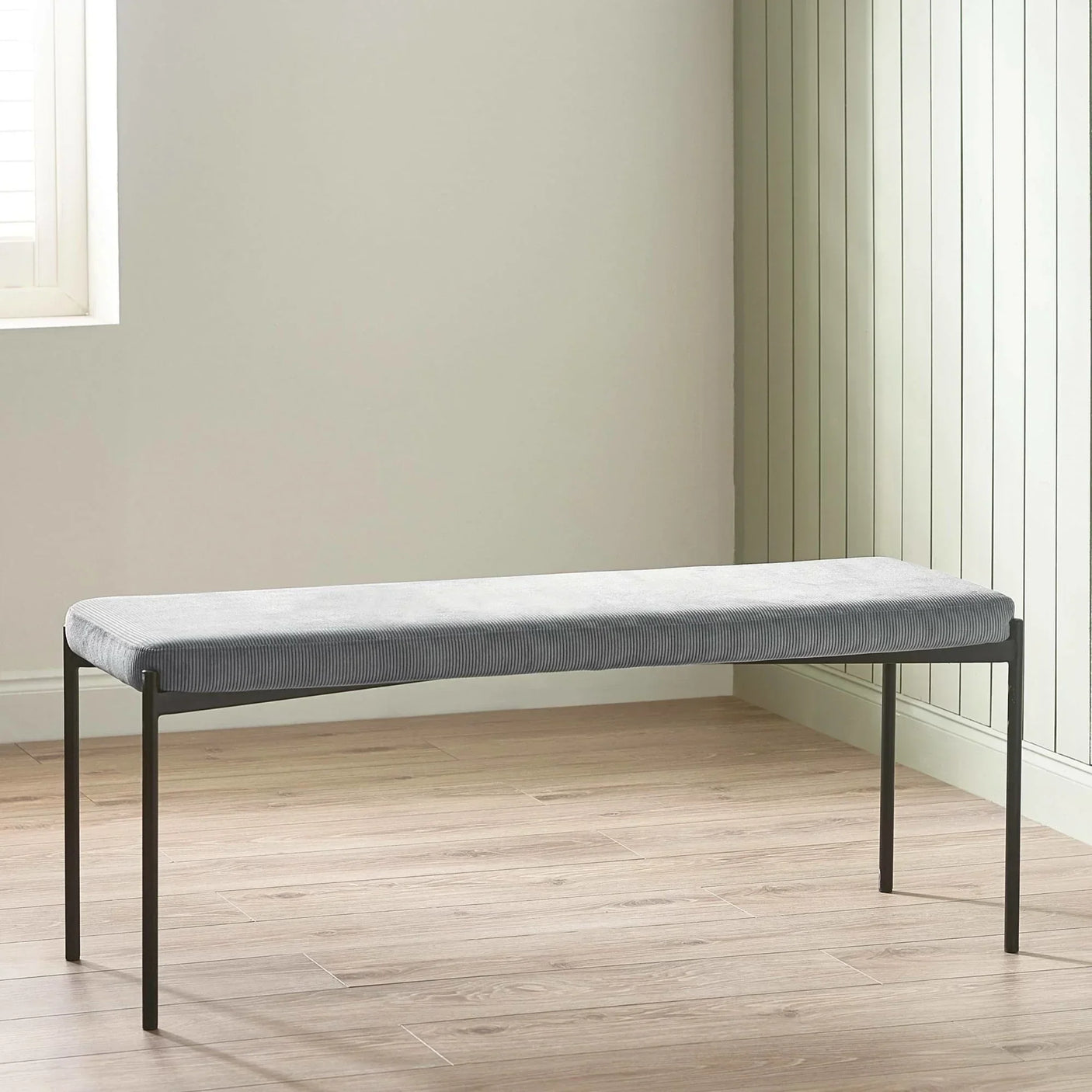 Grey fabric dining bench with slim black metal legs on wooden floor in modern room