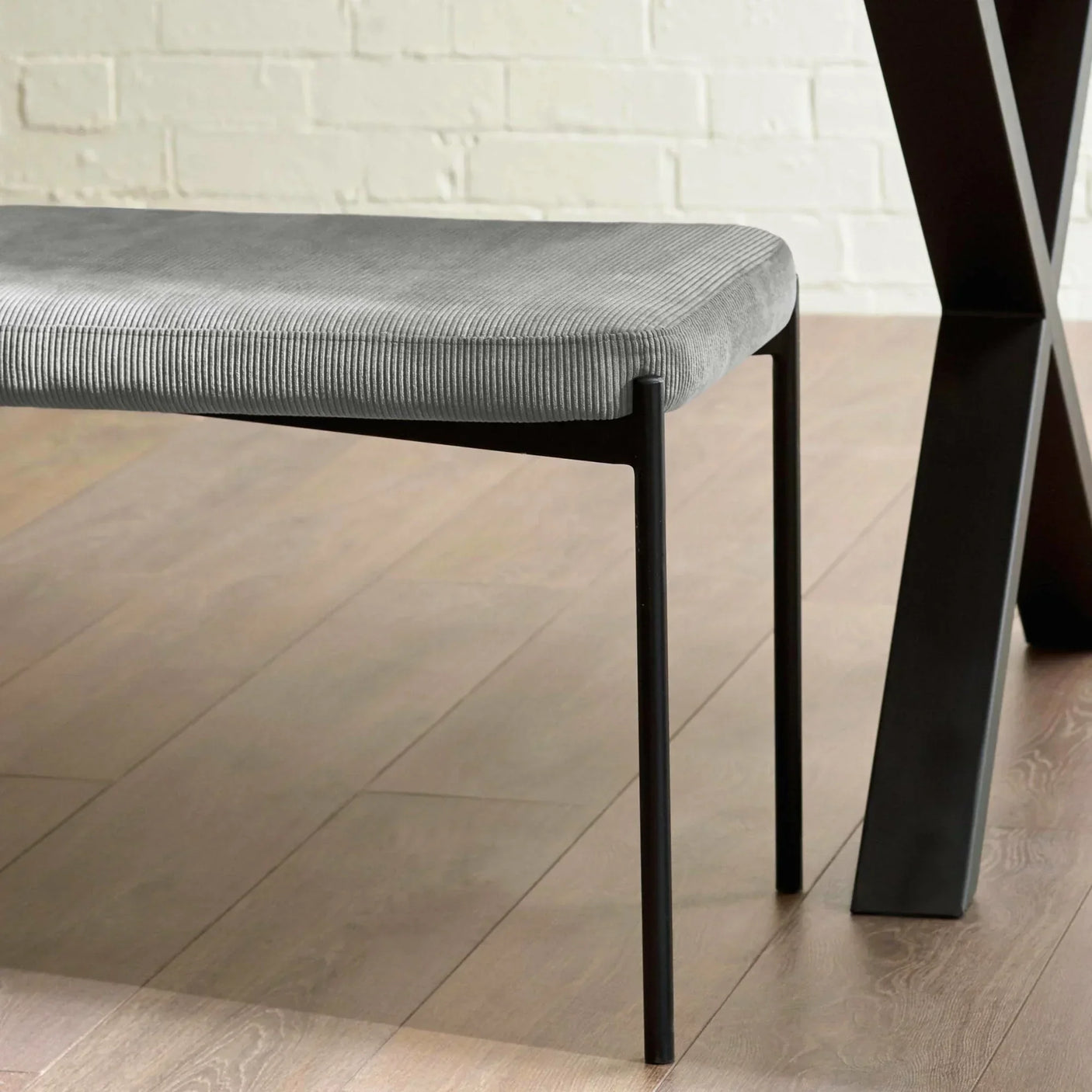 Grey fabric dining bench with slim black metal legs next to dark wood table on wood floor