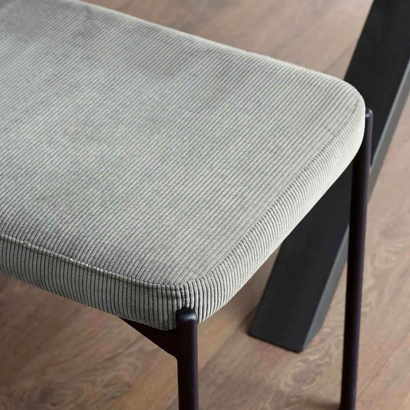 Close up of grey corduroy dining bench seat with black metal legs on wood floor