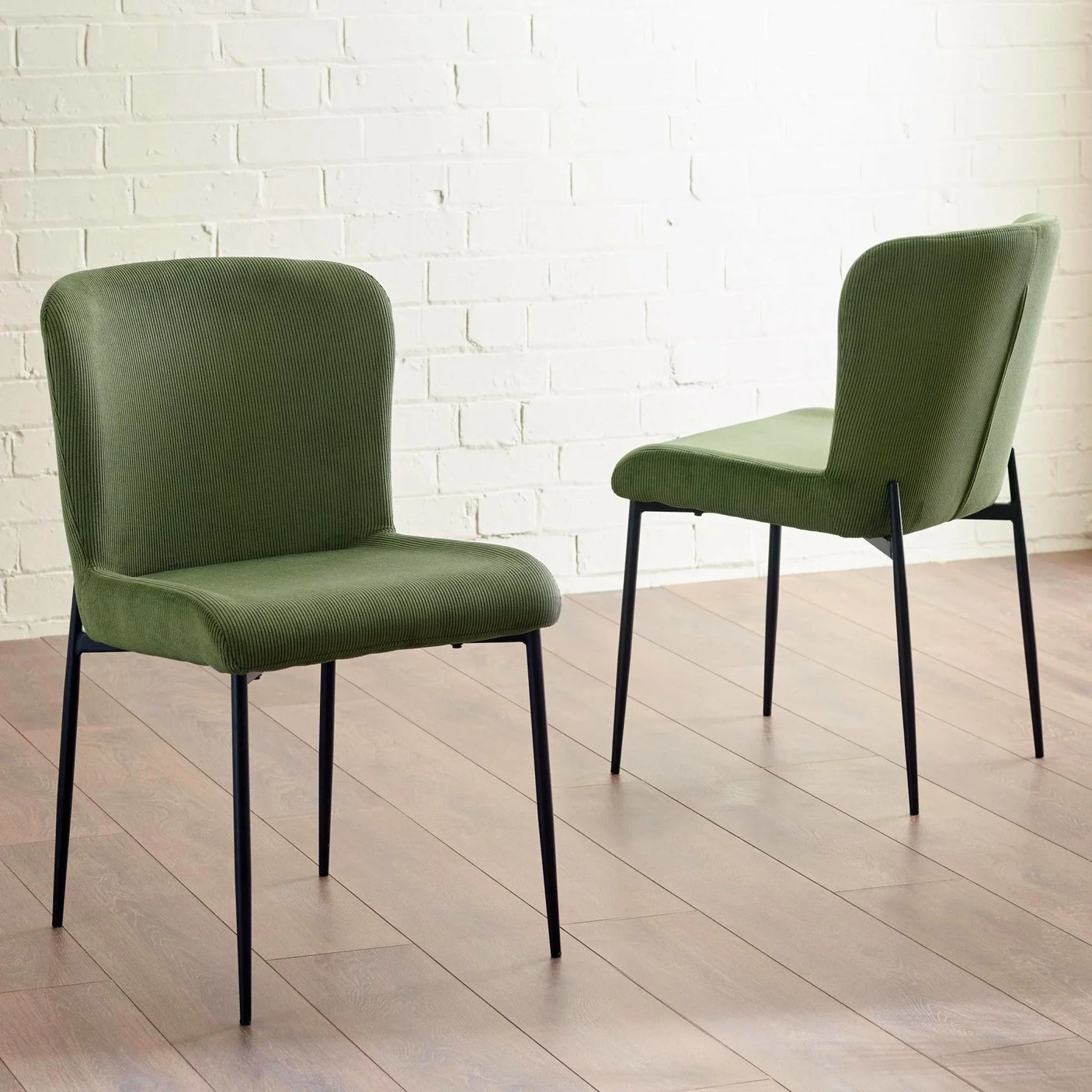 Green fabric dining chairs with black metal legs on wood floor against white brick wall