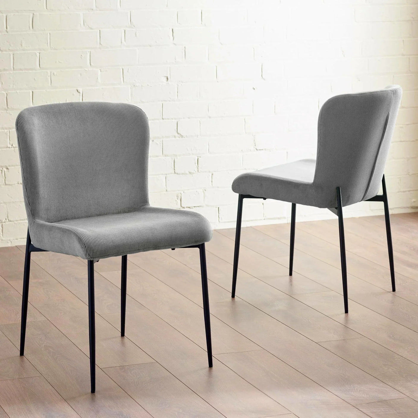 Pair of grey fabric dining chairs with black metal legs on wooden floor