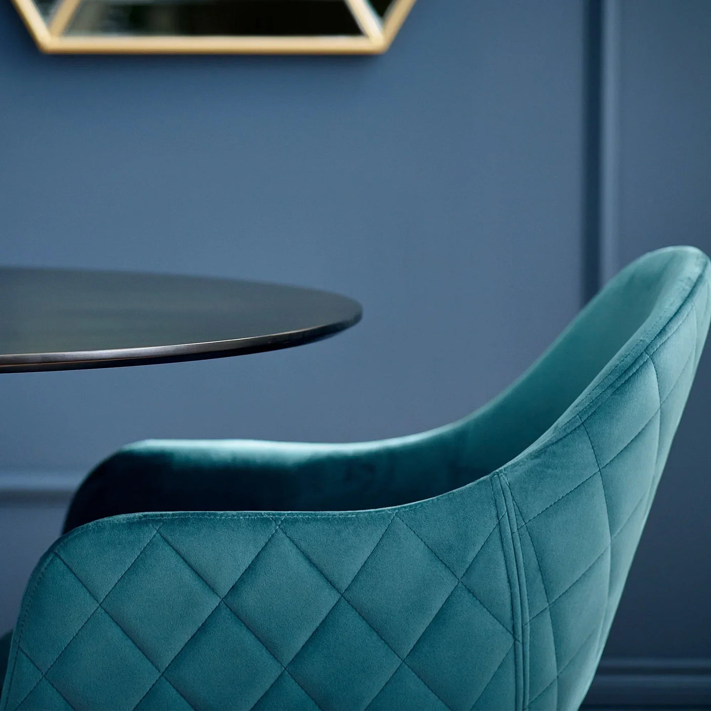 Teal velvet dining chair with diamond stitching beside round black dining table