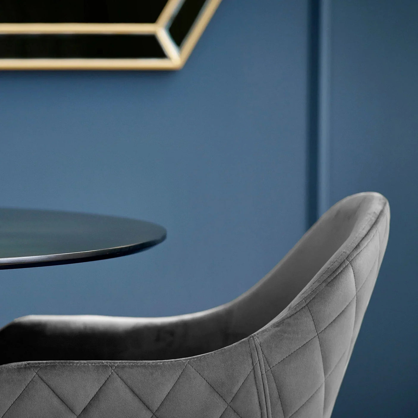 Grey velvet dining chair with diamond stitching beside round glass dining table