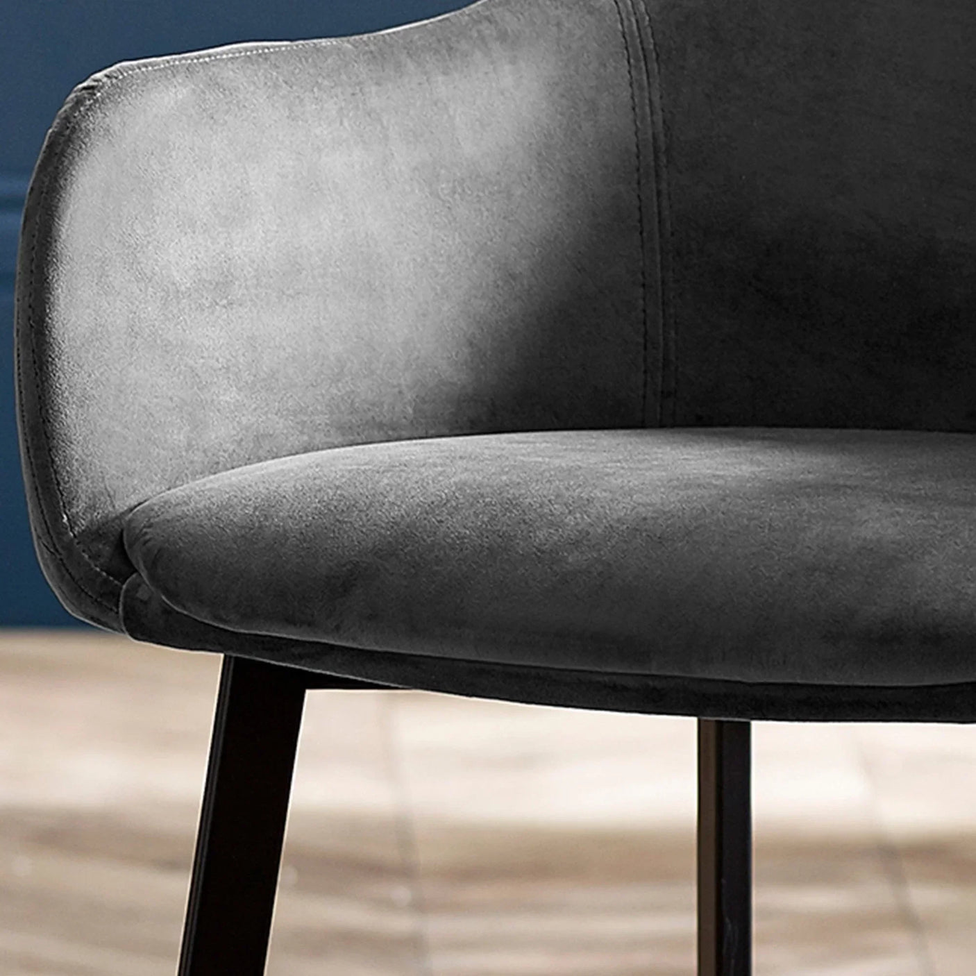 Grey velvet dining chair with curved backrest and black legs, close side view