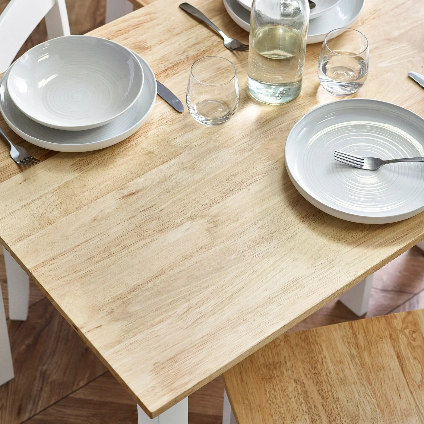Light wood small dining table with white legs set for two with plates and glasses
