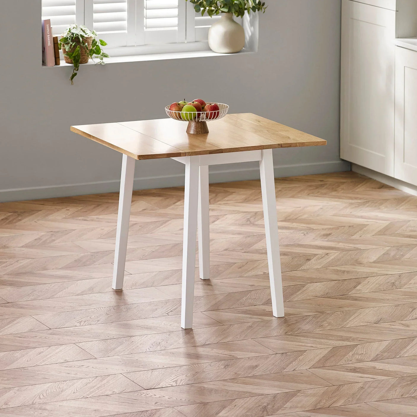 Square wooden dining table with white legs in a modern kitchen, fruit bowl on top