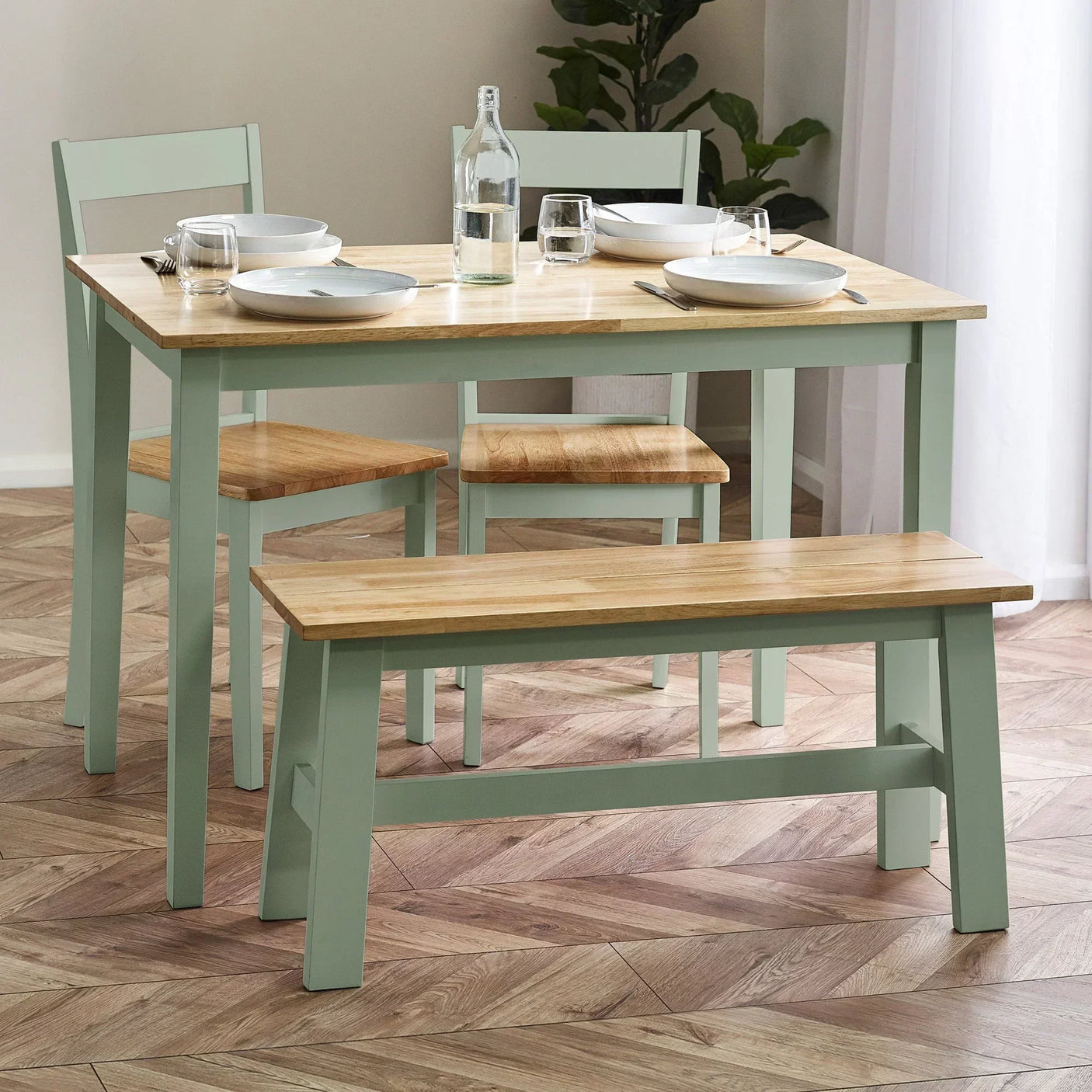 Light wood dining table set with two chairs and bench on chevron parquet floor