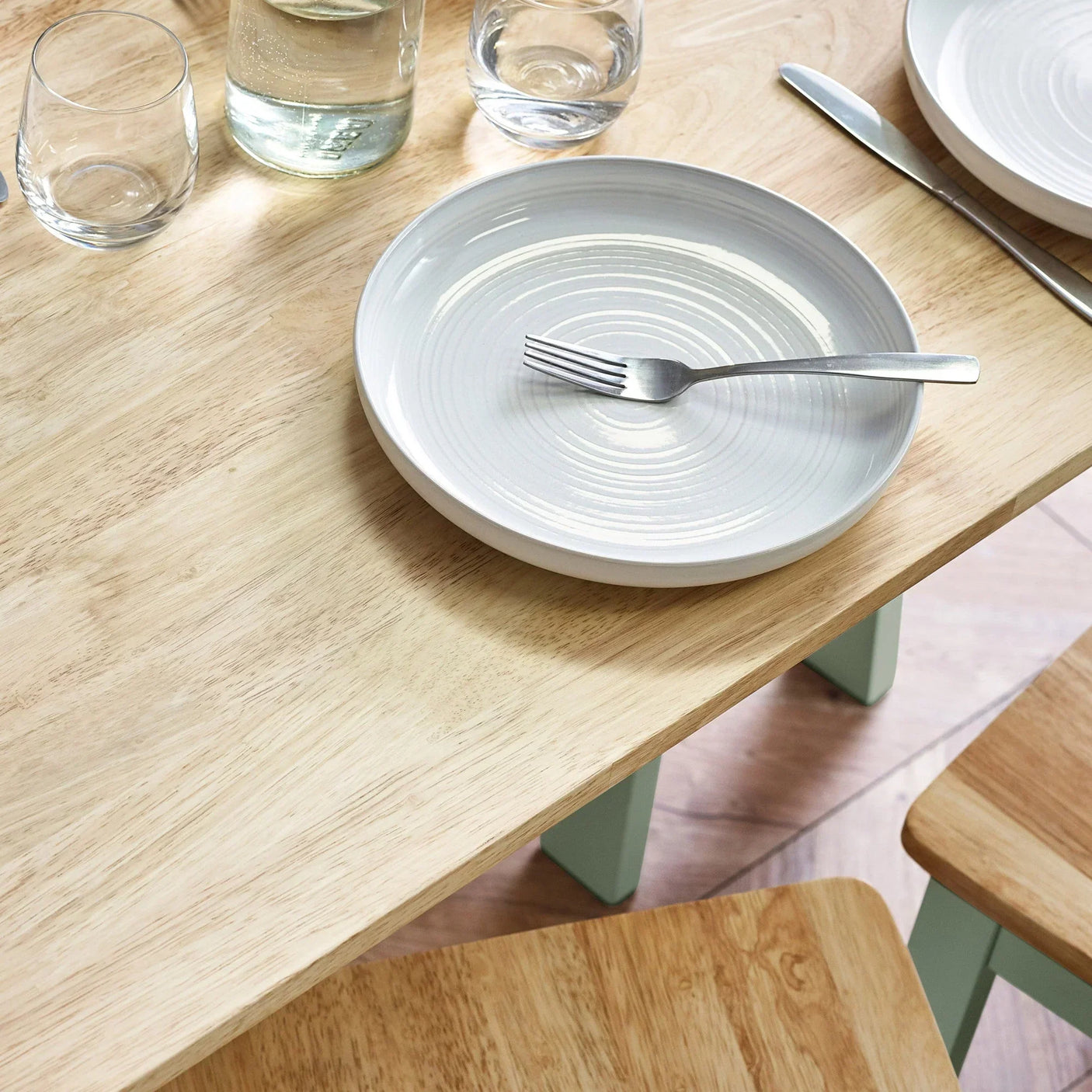 Light wood dining table set with ceramic plate, fork, glassware and matching chairs