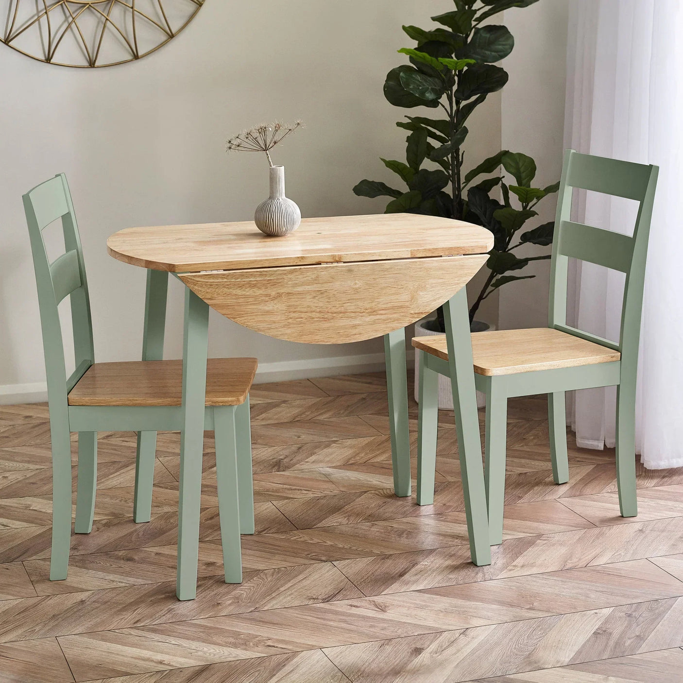 Drop leaf dining table set with light wood top and sage green chairs in bright room