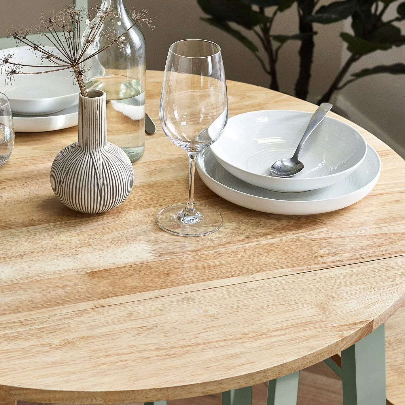 Light wood dining table set with plates, bowls, glassware and striped ceramic vase