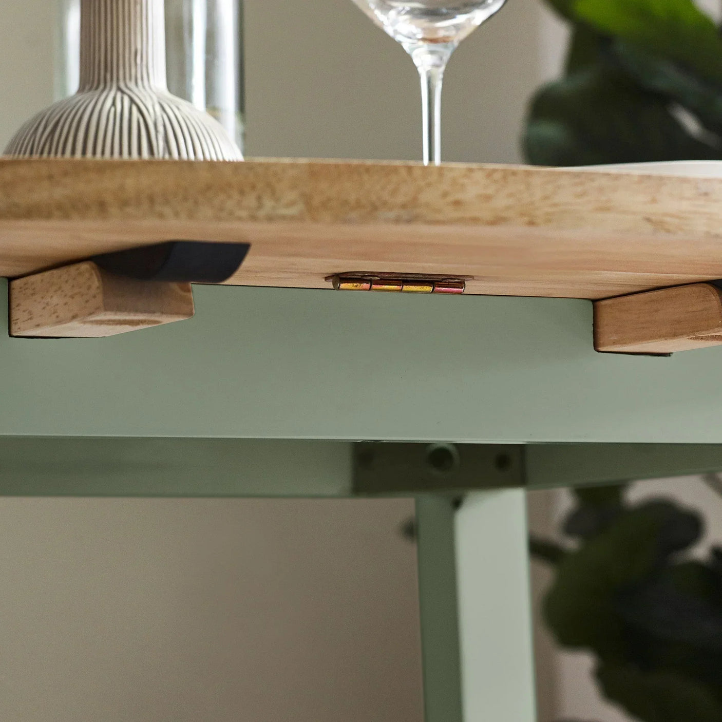 Light wood dining table closeup with green metal frame and decor accents