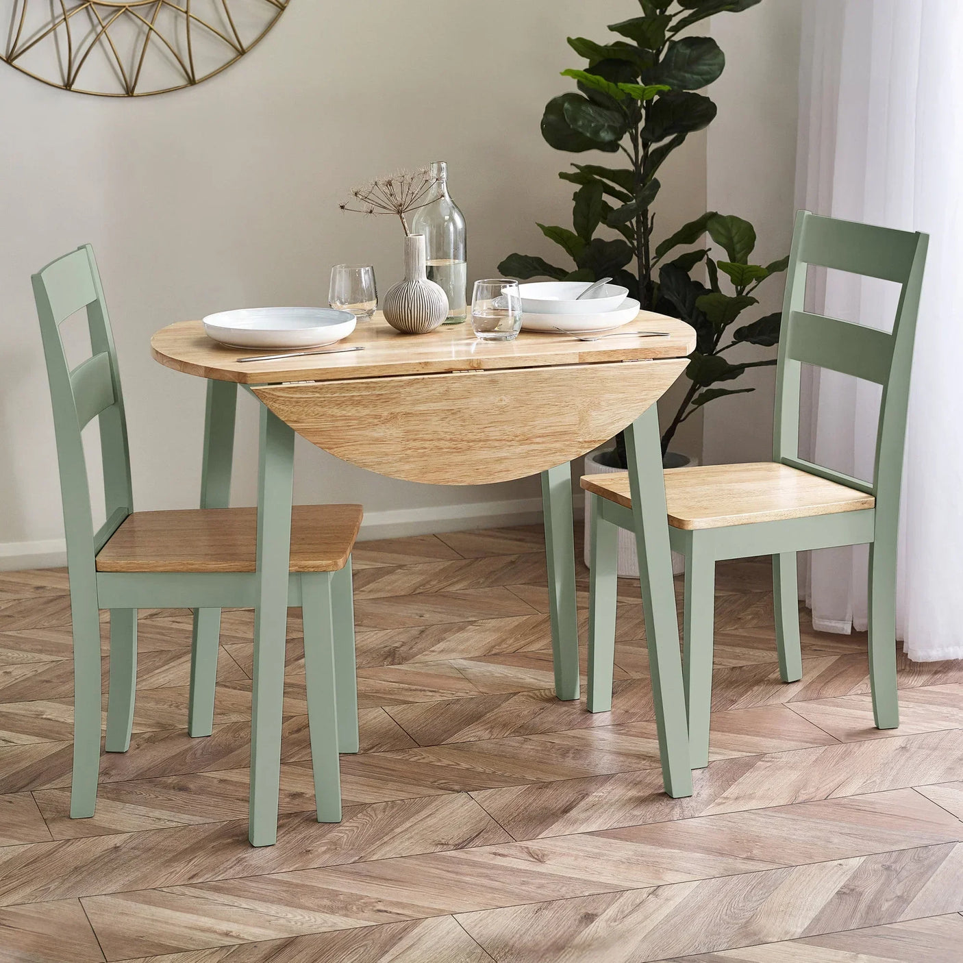 Round wood dining table with sage green legs and two matching chairs in a modern dining area