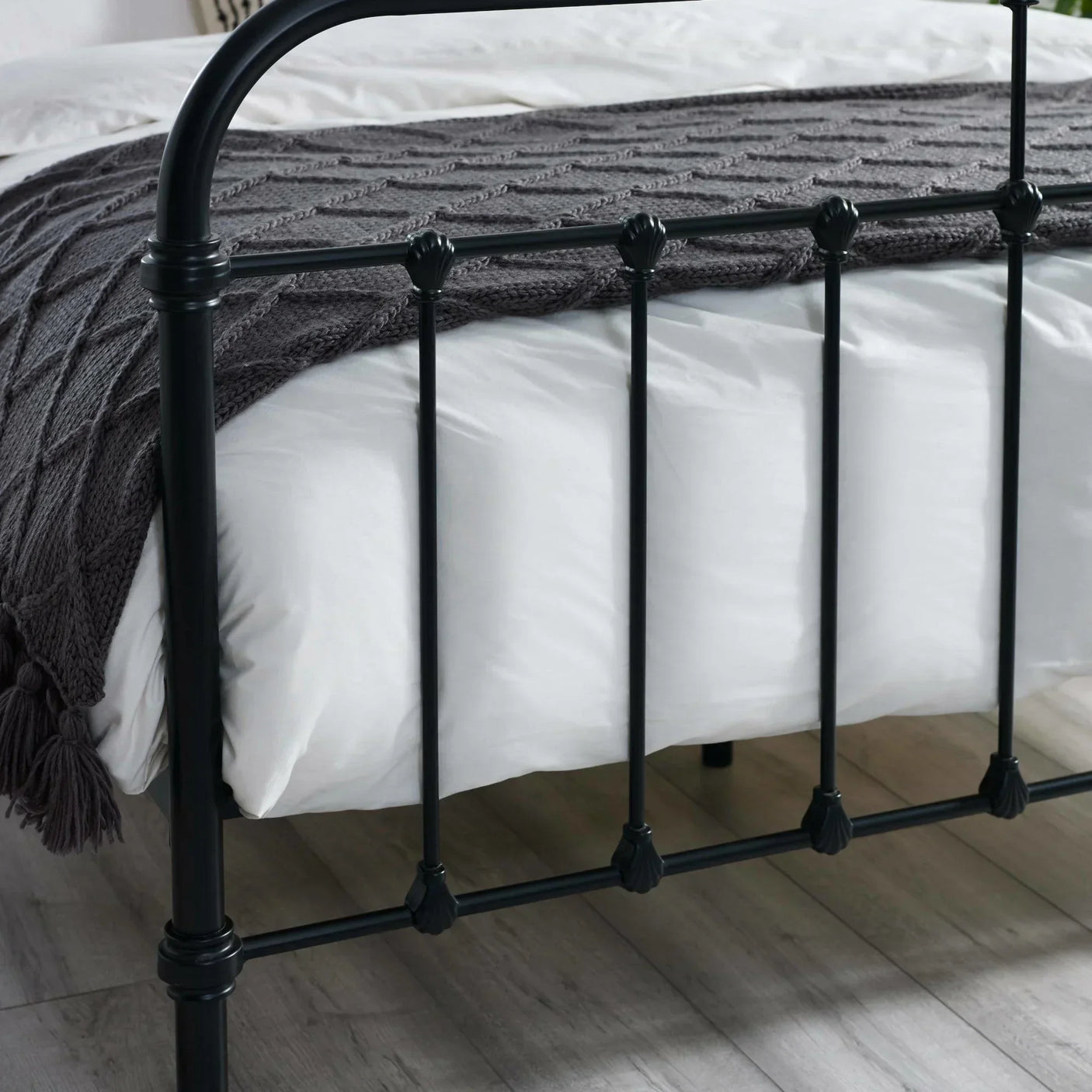 Black metal bed frame with decorative details and grey knitted throw on white bedding