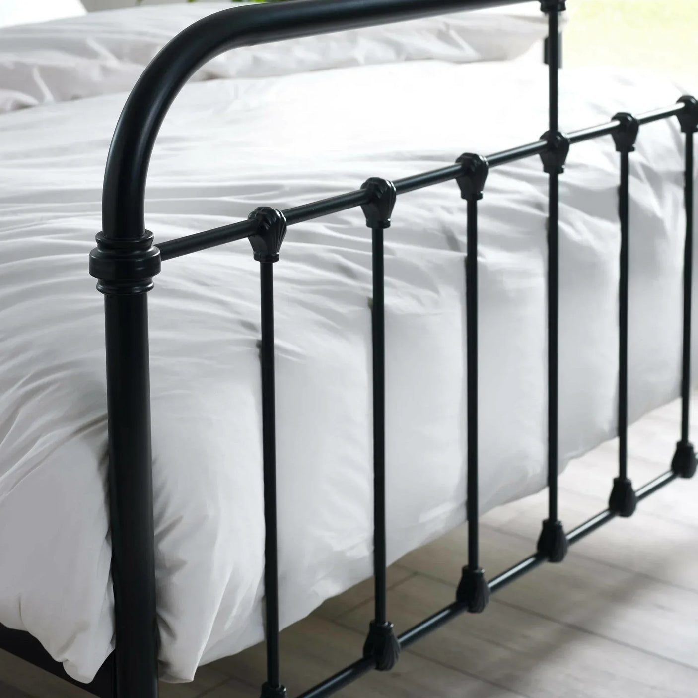 Black metal bed frame footboard with vertical bars and white bedding