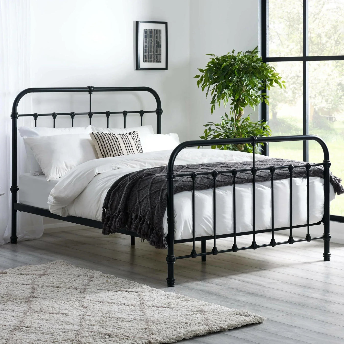 Black metal bed frame with white bedding in modern bedroom with large window and indoor plant