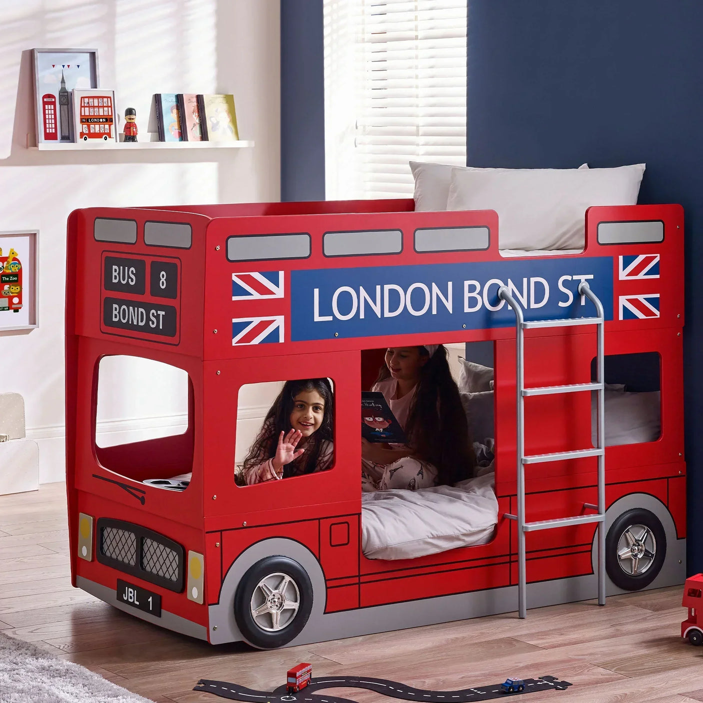 Red London bus bunk bed with ladder in kids' bedroom, two children inside, books on shelves