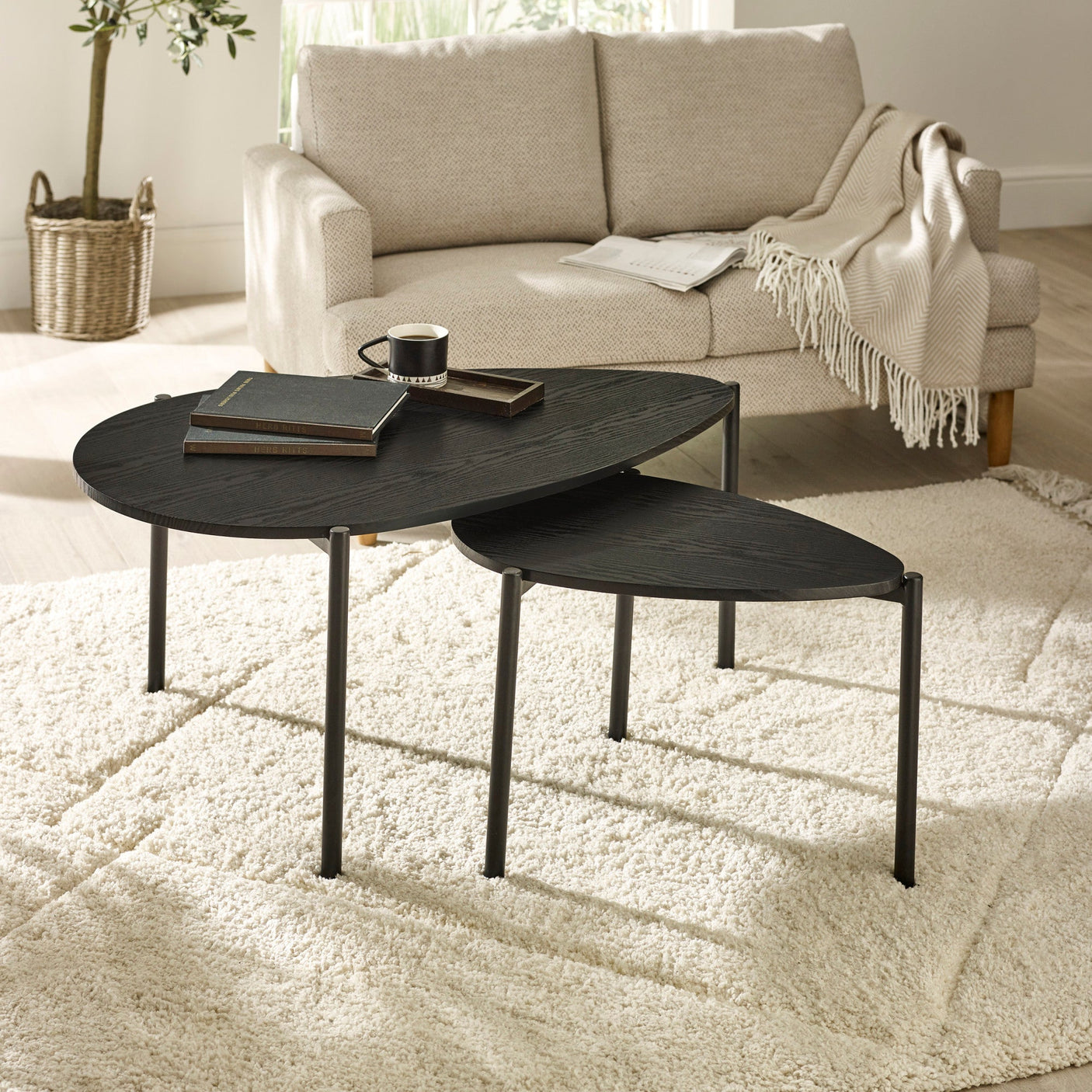Two black teardrop-shaped nesting coffee tables on fluffy beige carpet in front of beige sofa