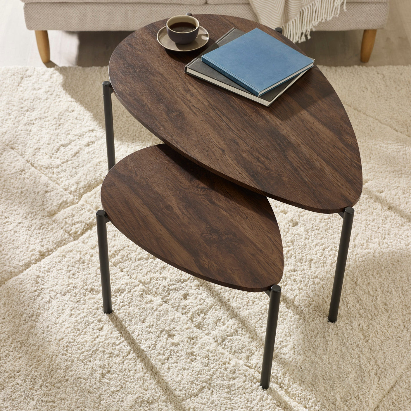 Two teardrop wooden nesting coffee tables with dark wood top, black legs, on textured cream carpet