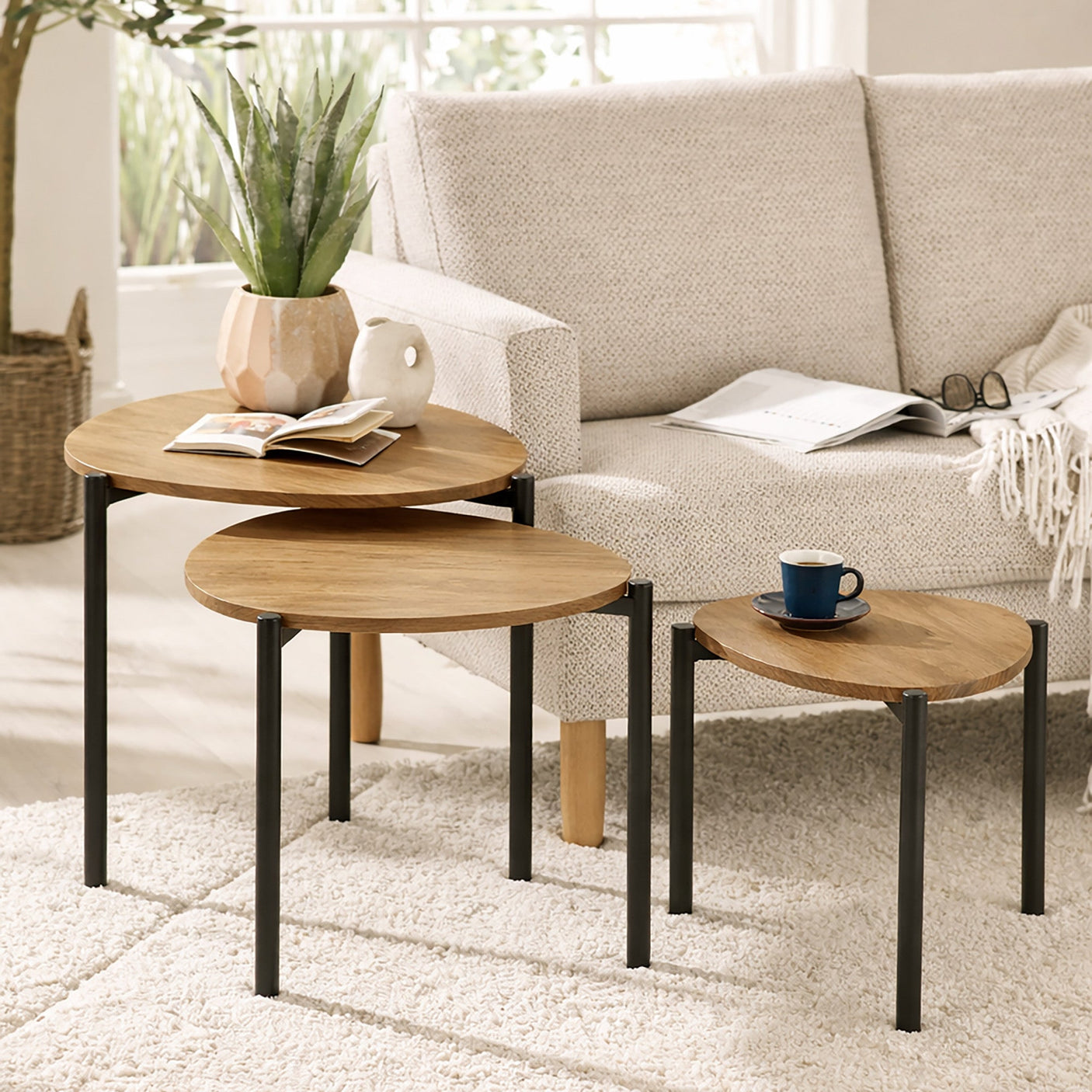 Nesting tables with light wood teardrop tops and black metal legs on cream rug beside sofa.
