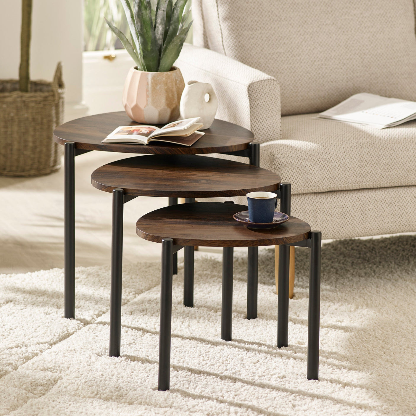 Three dark wood teardrop nesting side tables in living room with sofa, plant, book, cup, and soft white rug.