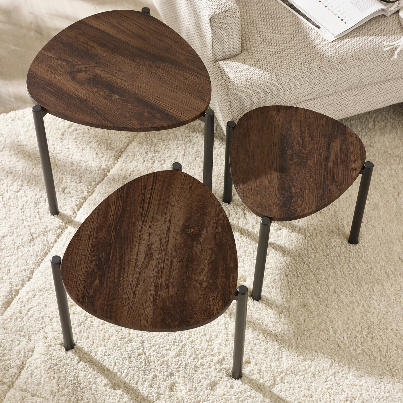 Top view of three dark wood teardrop nesting side tables with black metal legs arranged on soft white rug.