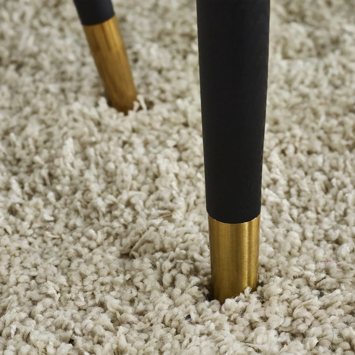 Black tapered dining table legs with gold metal caps on beige textured carpet