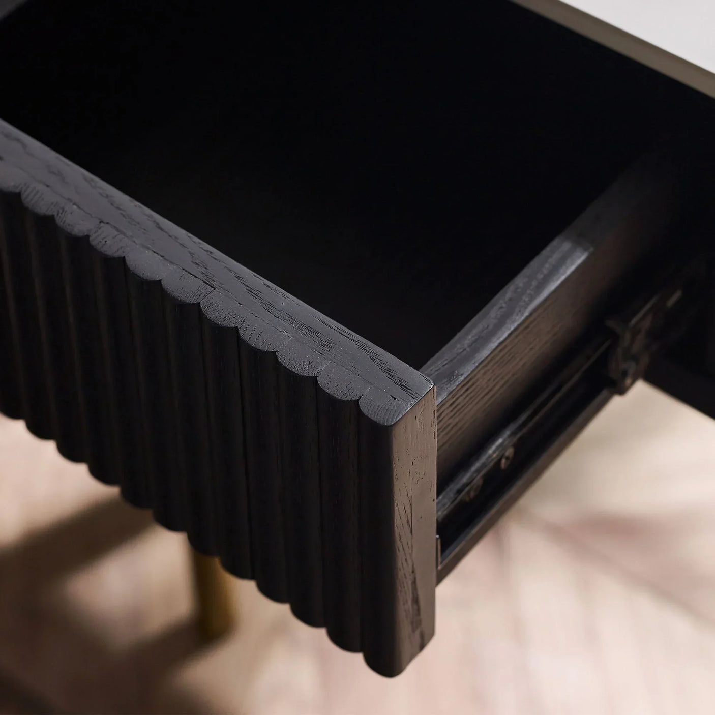 Black fluted lamp table with stone top and open drawer detail on wood floor