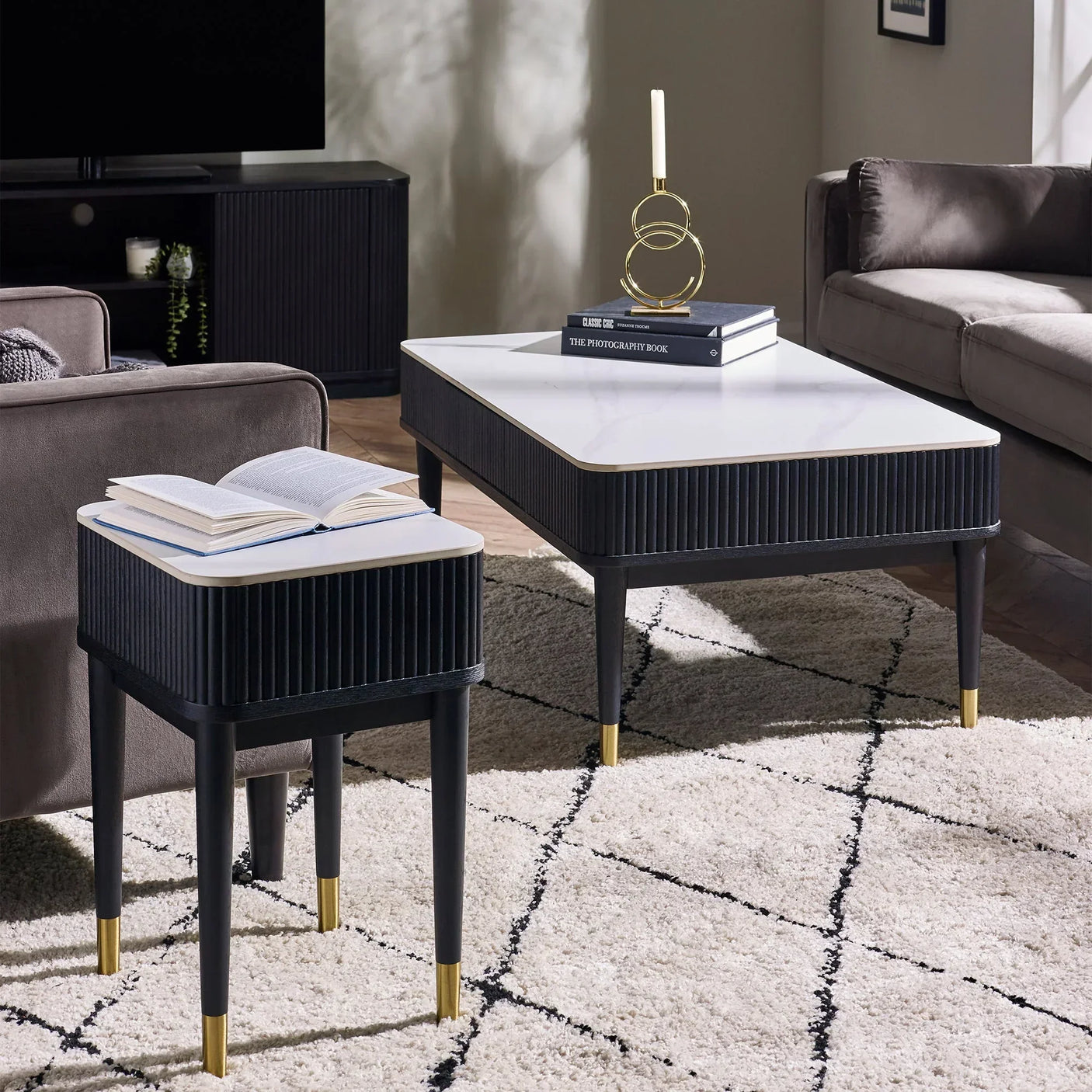 Black fluted stone top lamp table with drawer, gold-capped legs, beside modern sofa