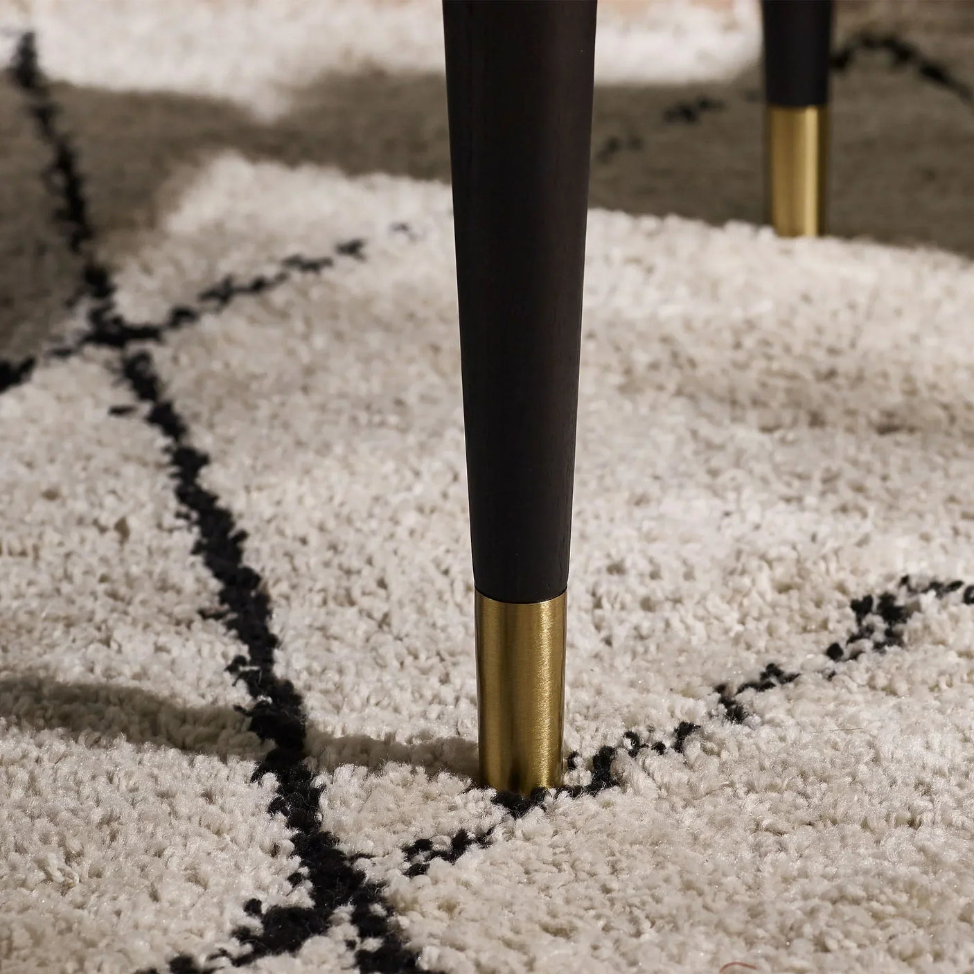 Black fluted coffee table leg with gold tip on cream rug with black lines