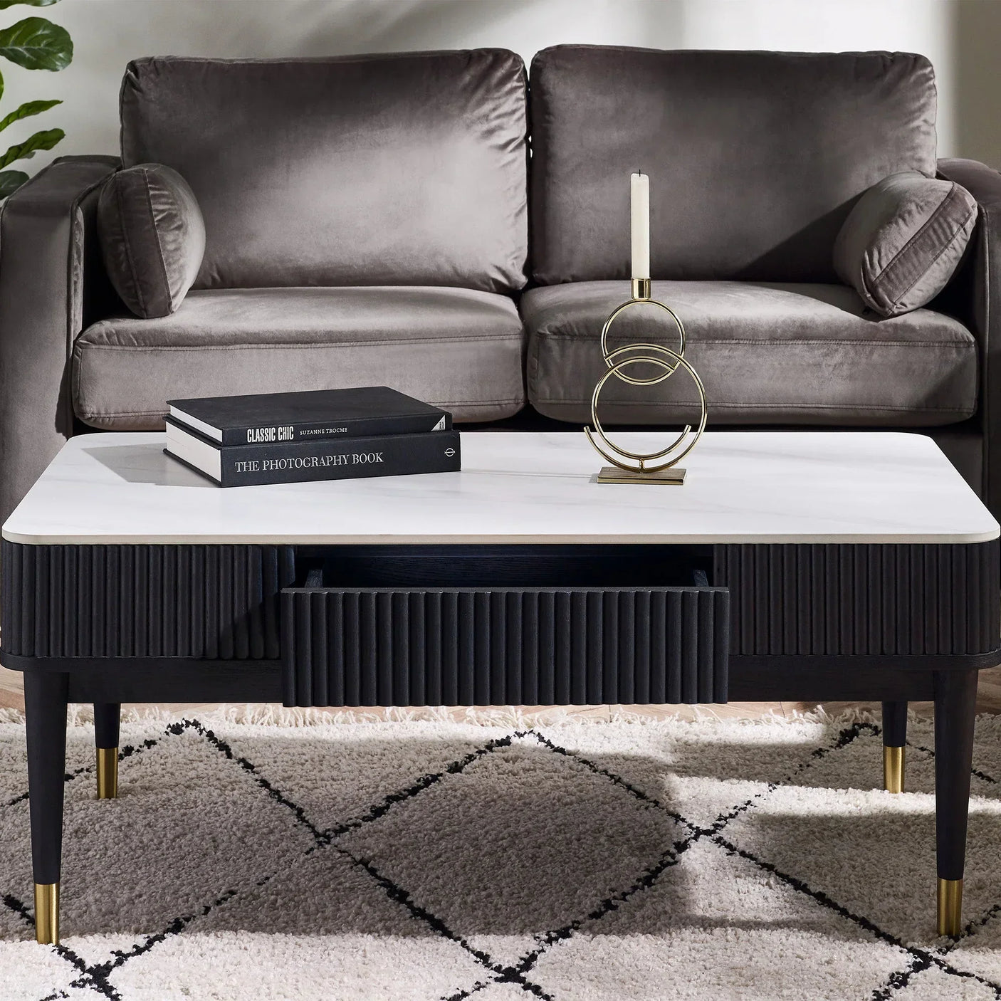 Black fluted coffee table with stone top and drawer in front of grey sofa on patterned rug