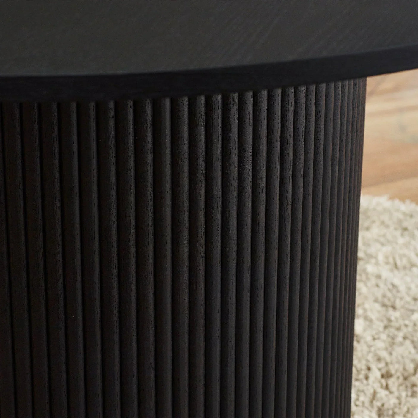 Black fluted round dining table base with vertical ridges on wooden floor near rug