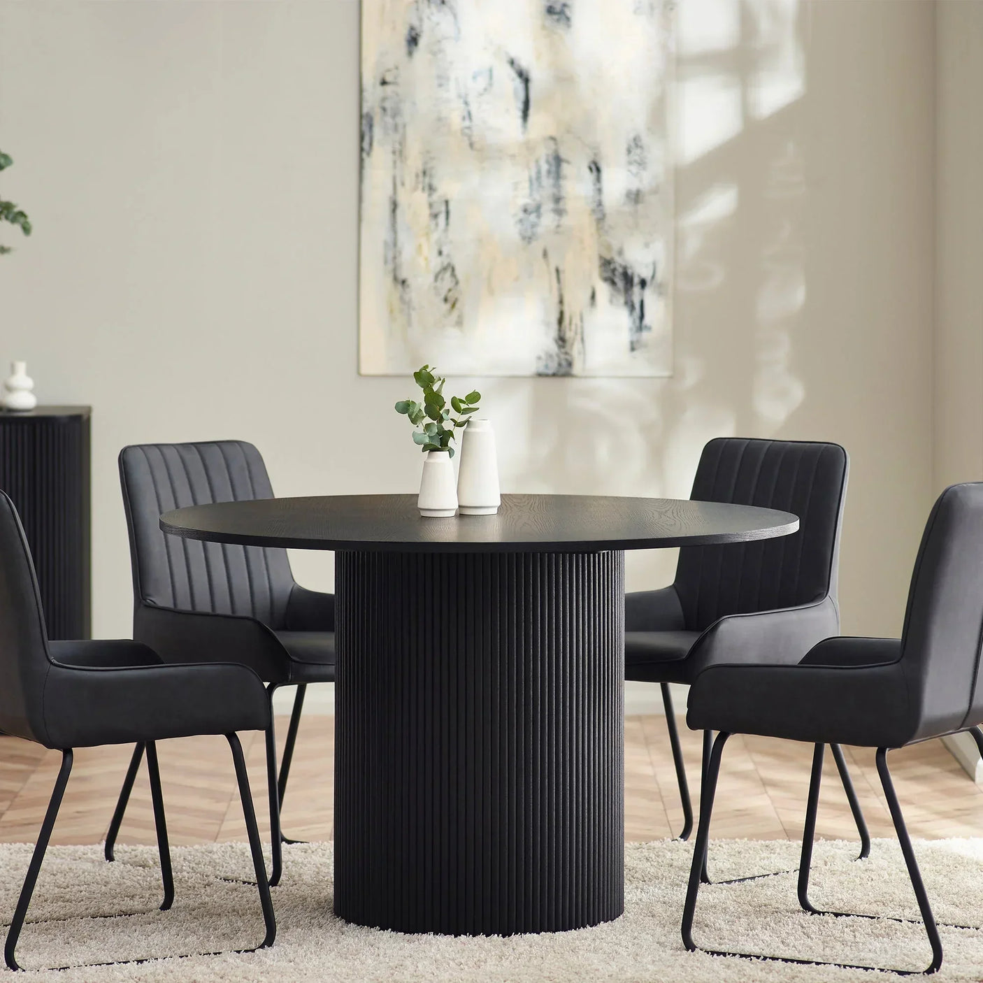 Black fluted round dining table with four black chairs on a cream rug in modern dining room