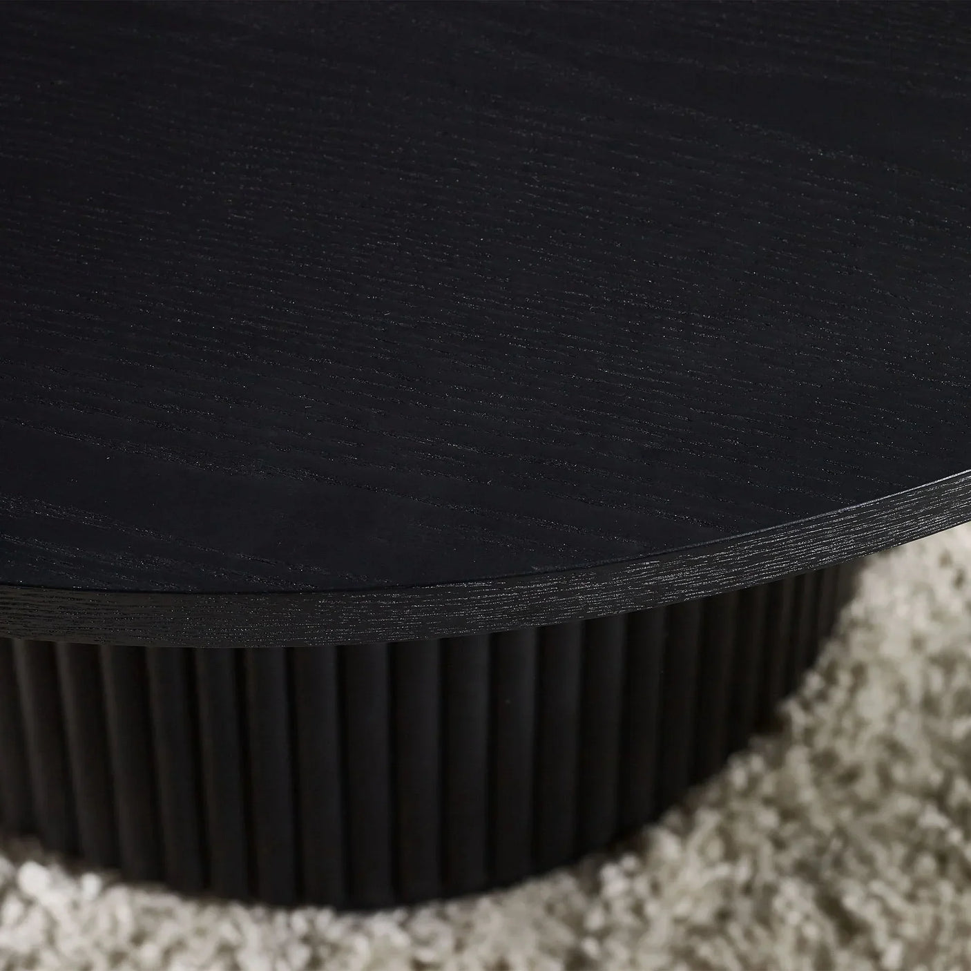 Black fluted round coffee table close-up showing textured wood grain and ribbed base on rug