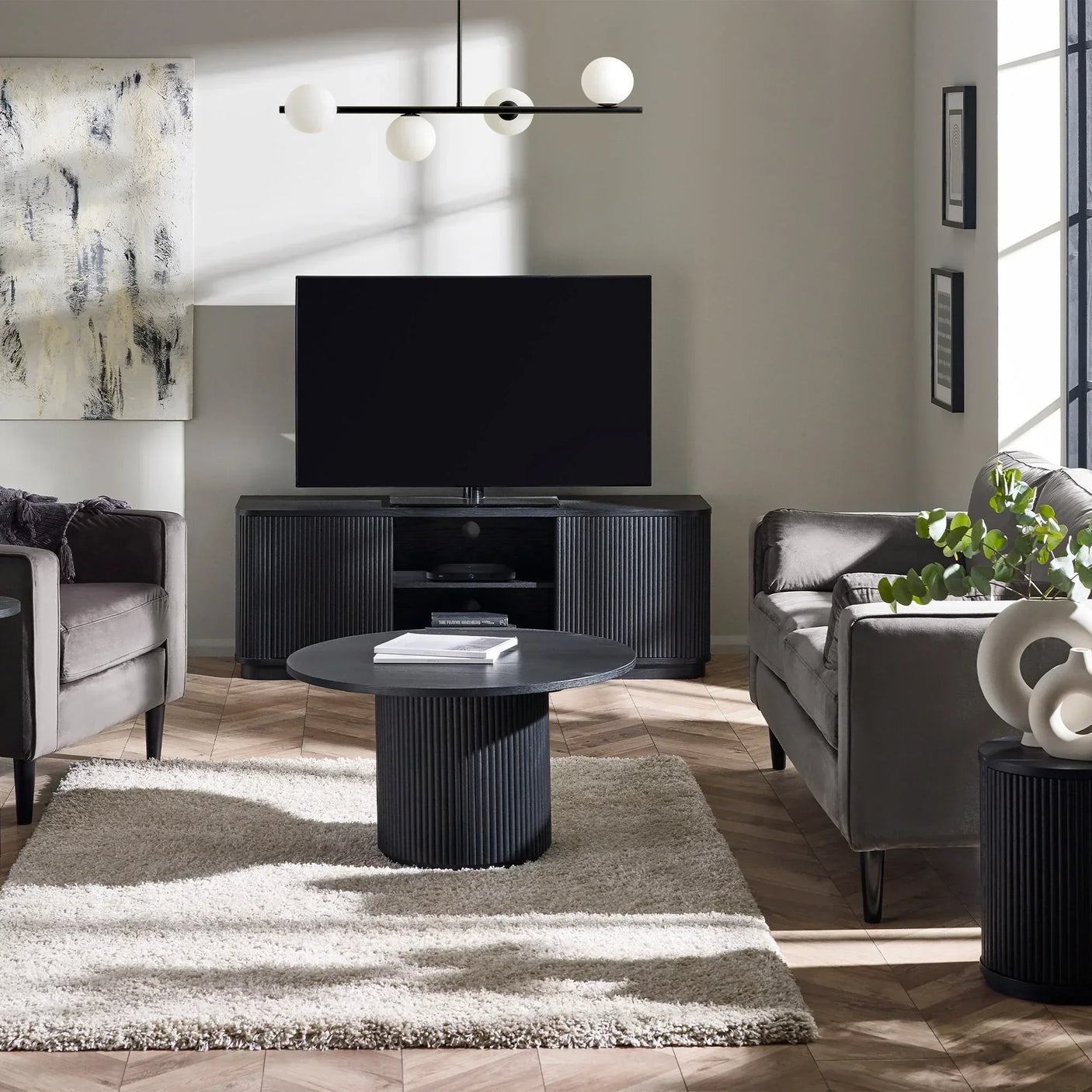 Black fluted round coffee table on cream rug in modern living room with grey sofas