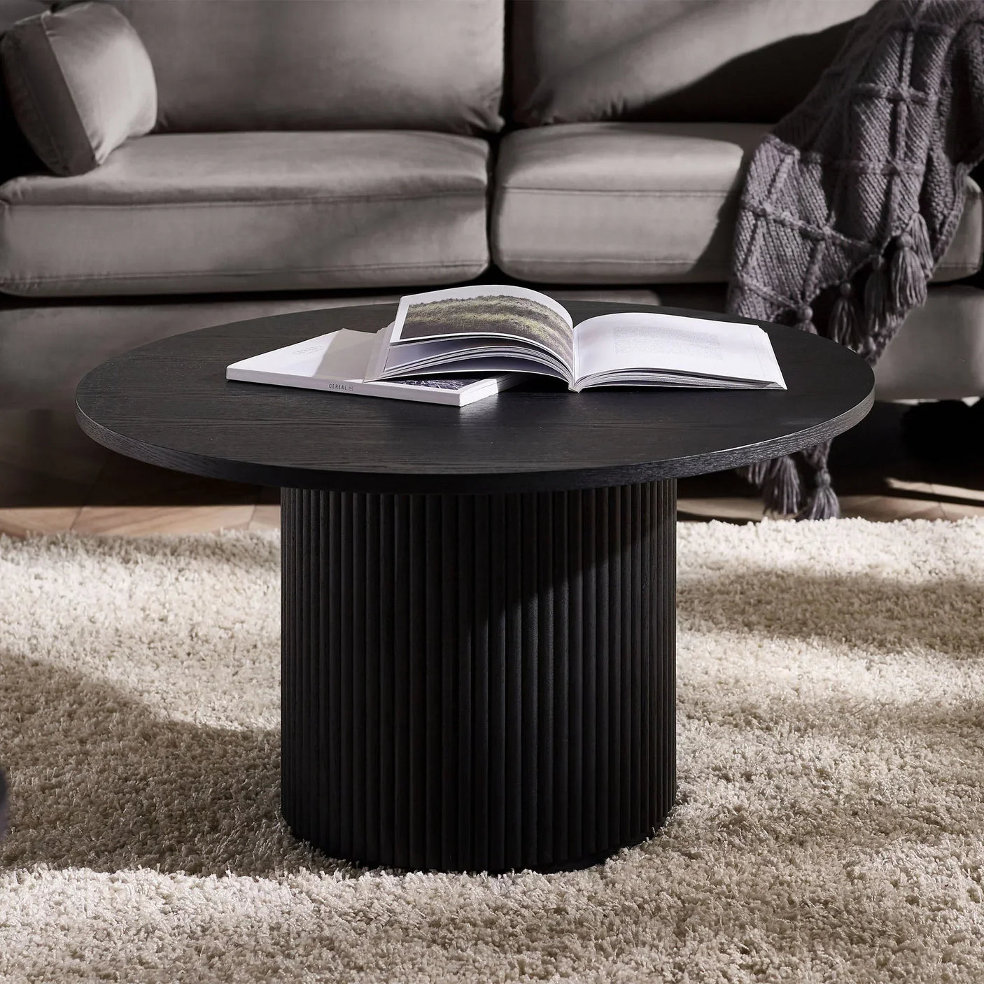 Black fluted round coffee table with open book in modern living room setting