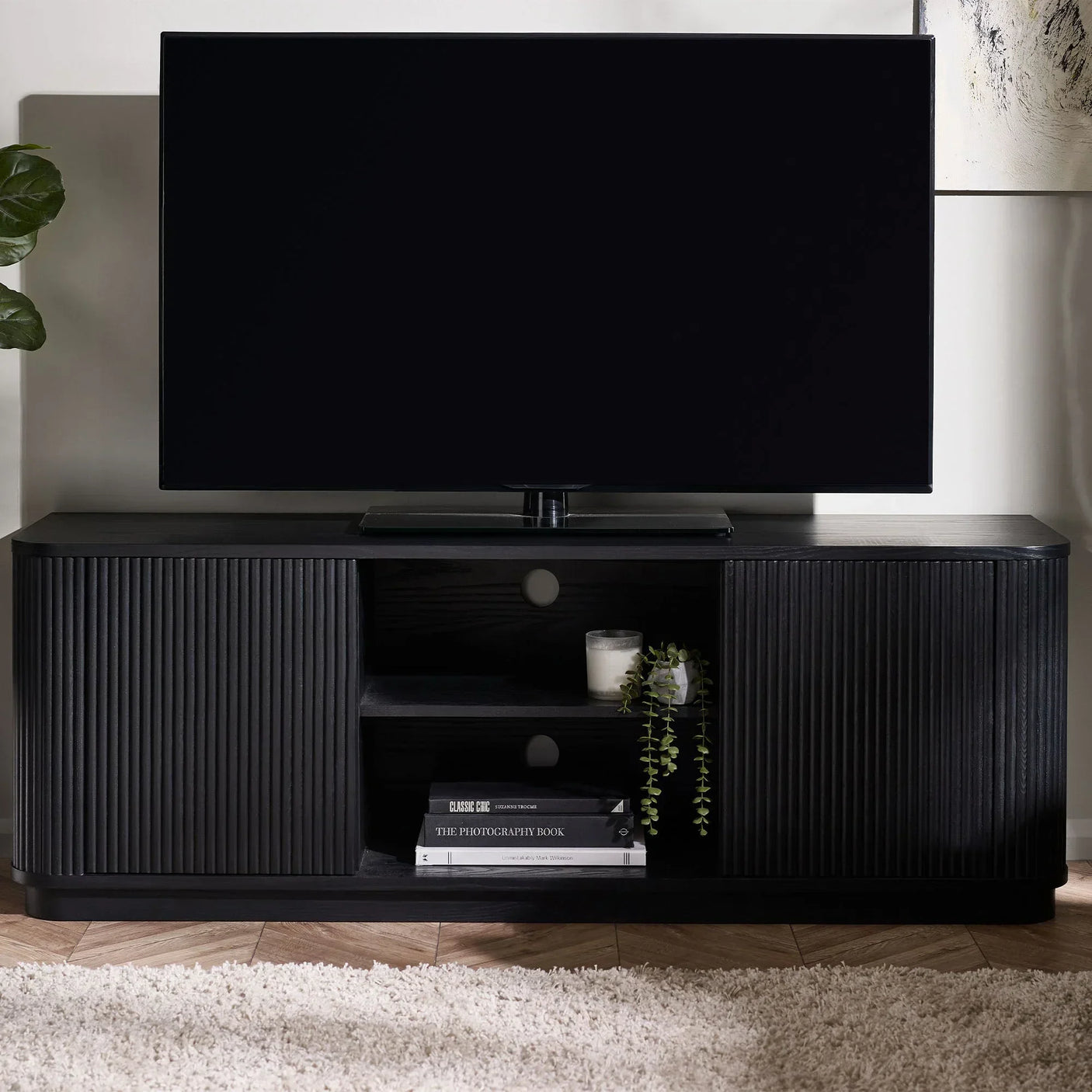 Black fluted TV unit with open shelving, books, candle, and a TV on top in a living room