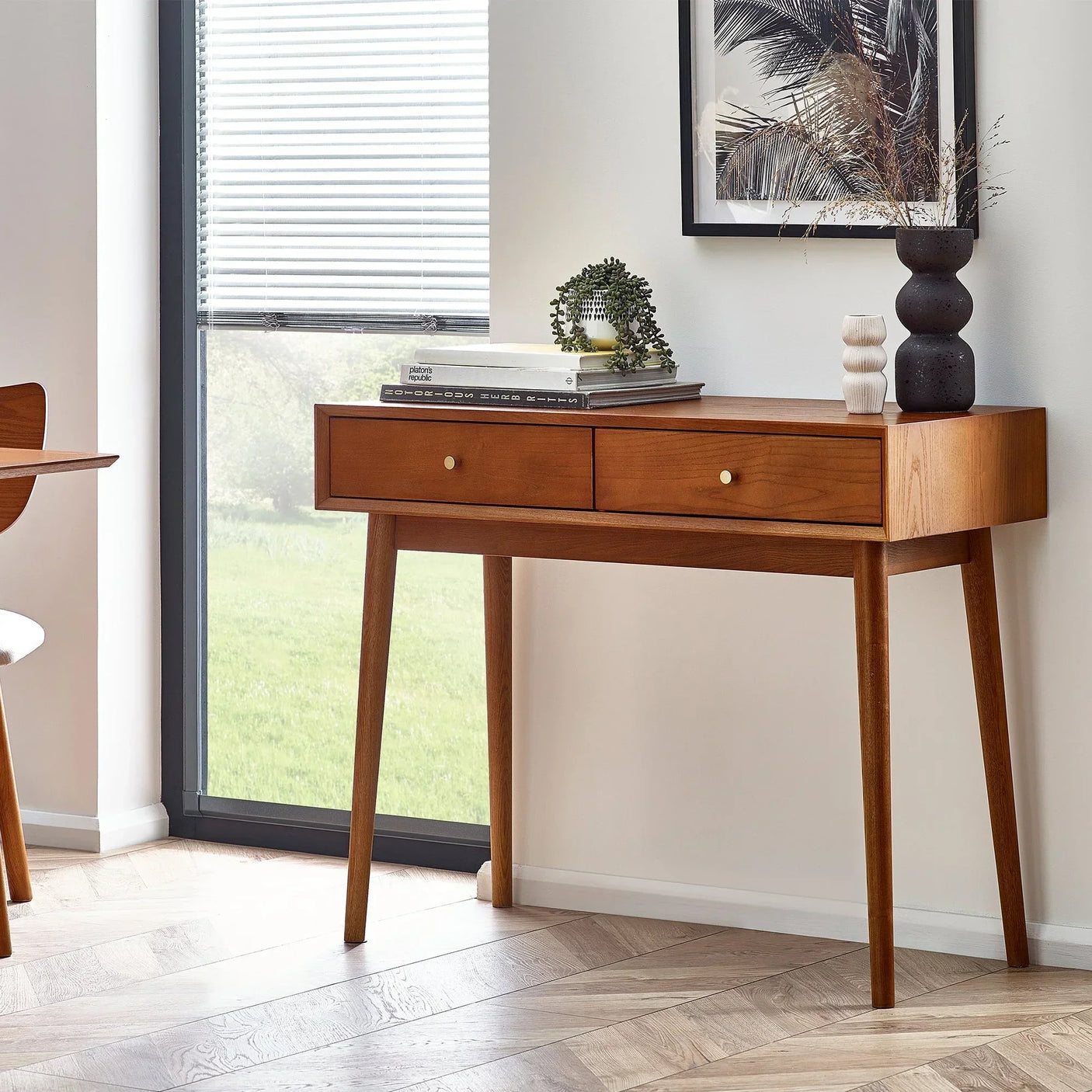 Wood writing desk with two drawers, angled legs, styled with decor in a bright room