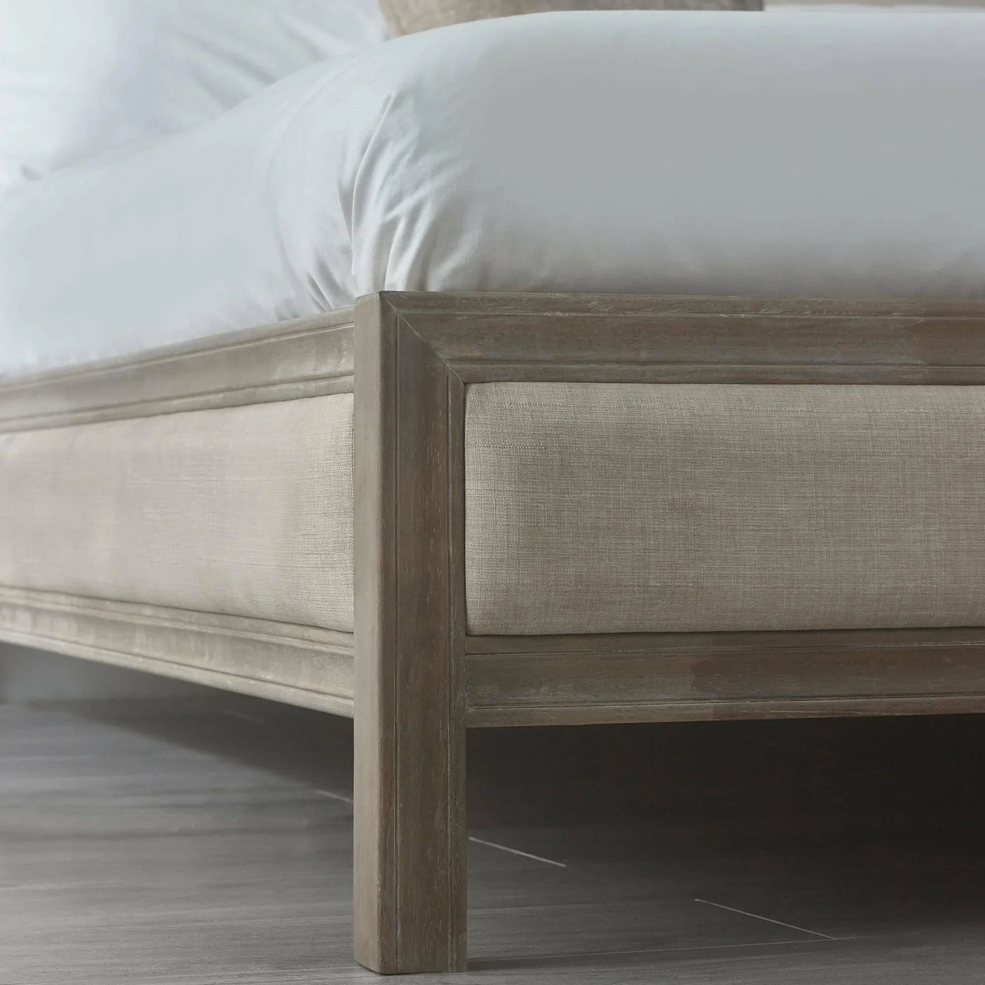 Closeup of upholstered bed frame with light wood and beige fabric on wooden floor