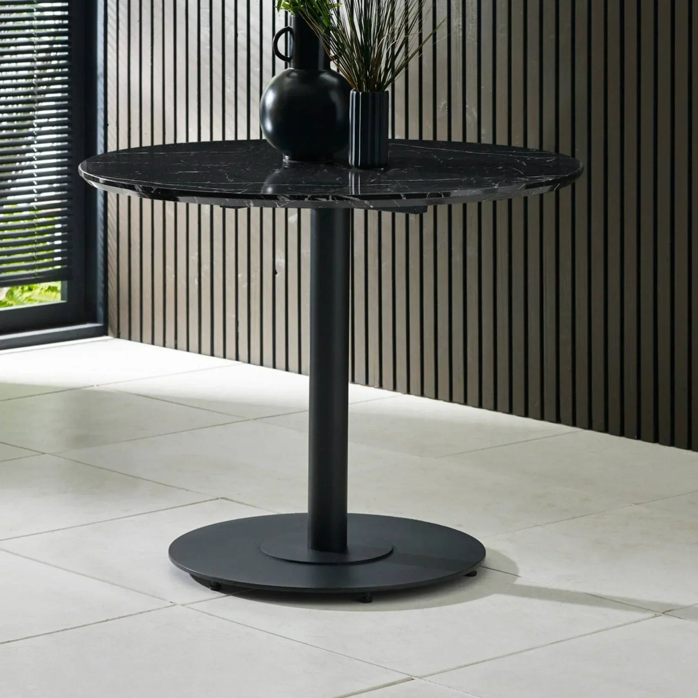 Round black marble dining table with central metal pedestal base in modern room