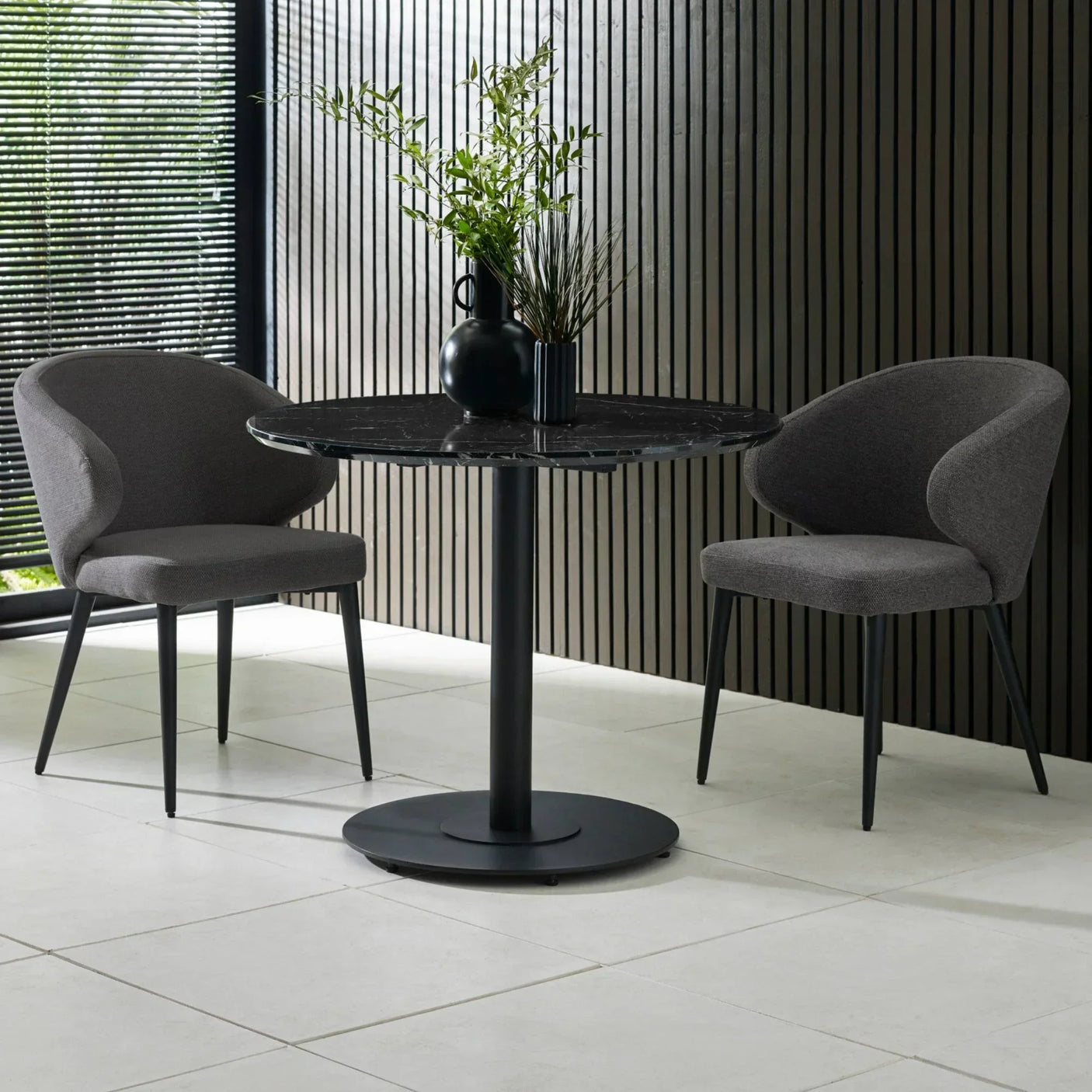 Round black dining table with marble top and two grey fabric chairs in modern setting