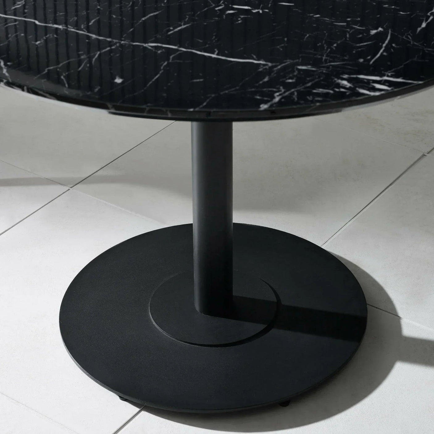 Round black marble dining table with central metal pedestal base on tiled floor