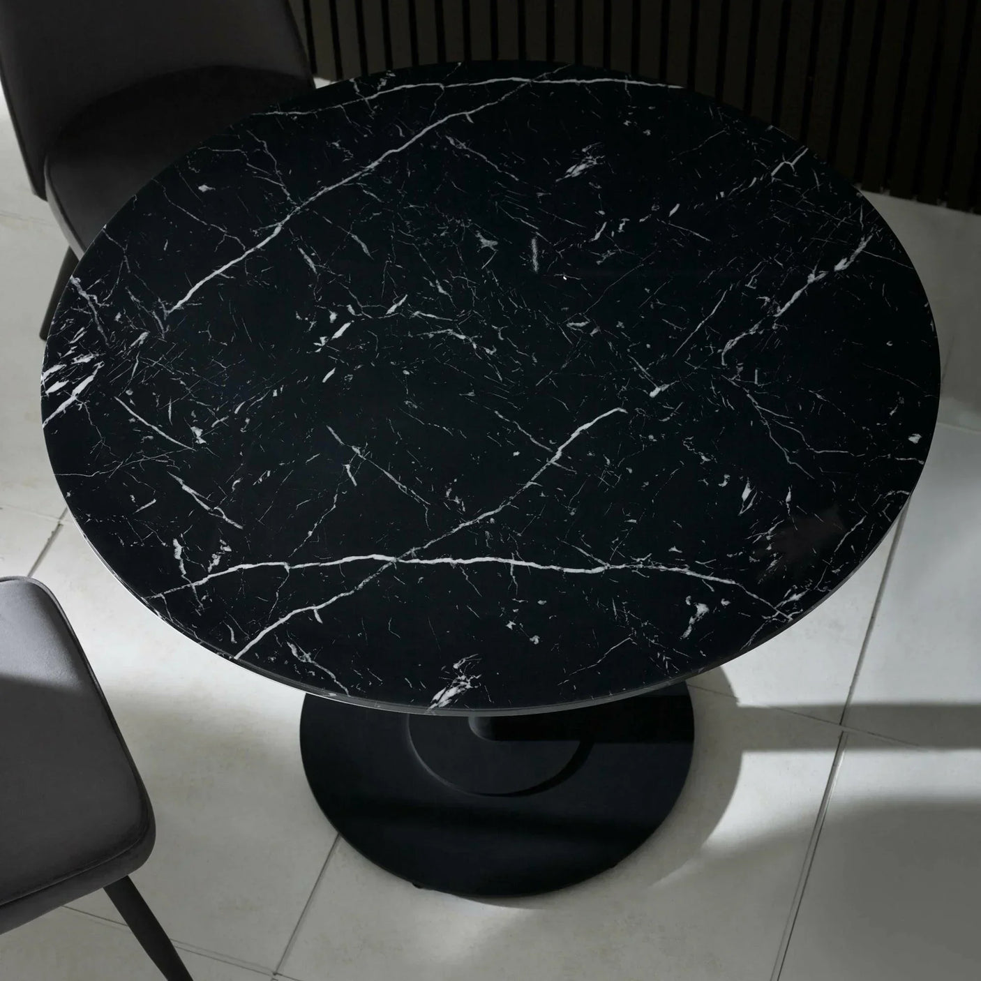 Round black marble dining table with white veining and pedestal base on tiled floor