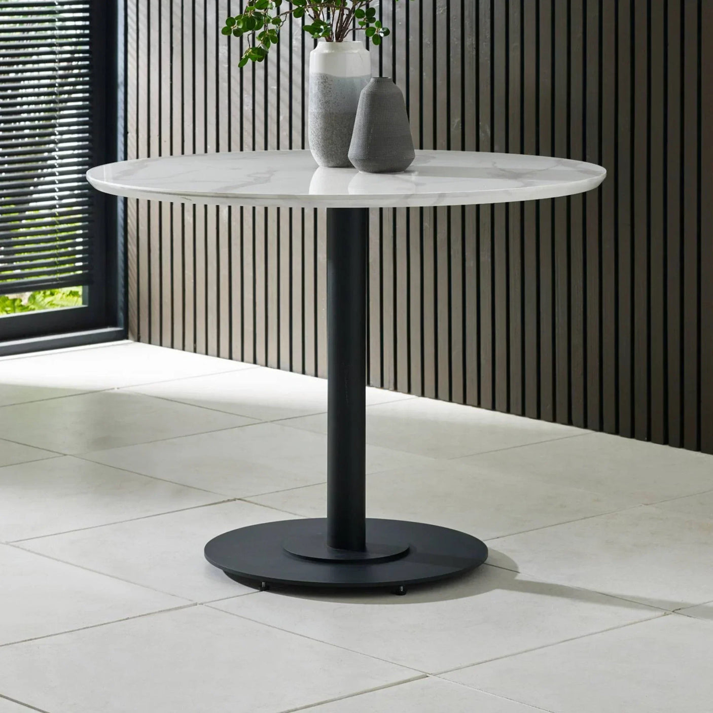 Round marble dining table with black metal pedestal base, styled with vases and greenery