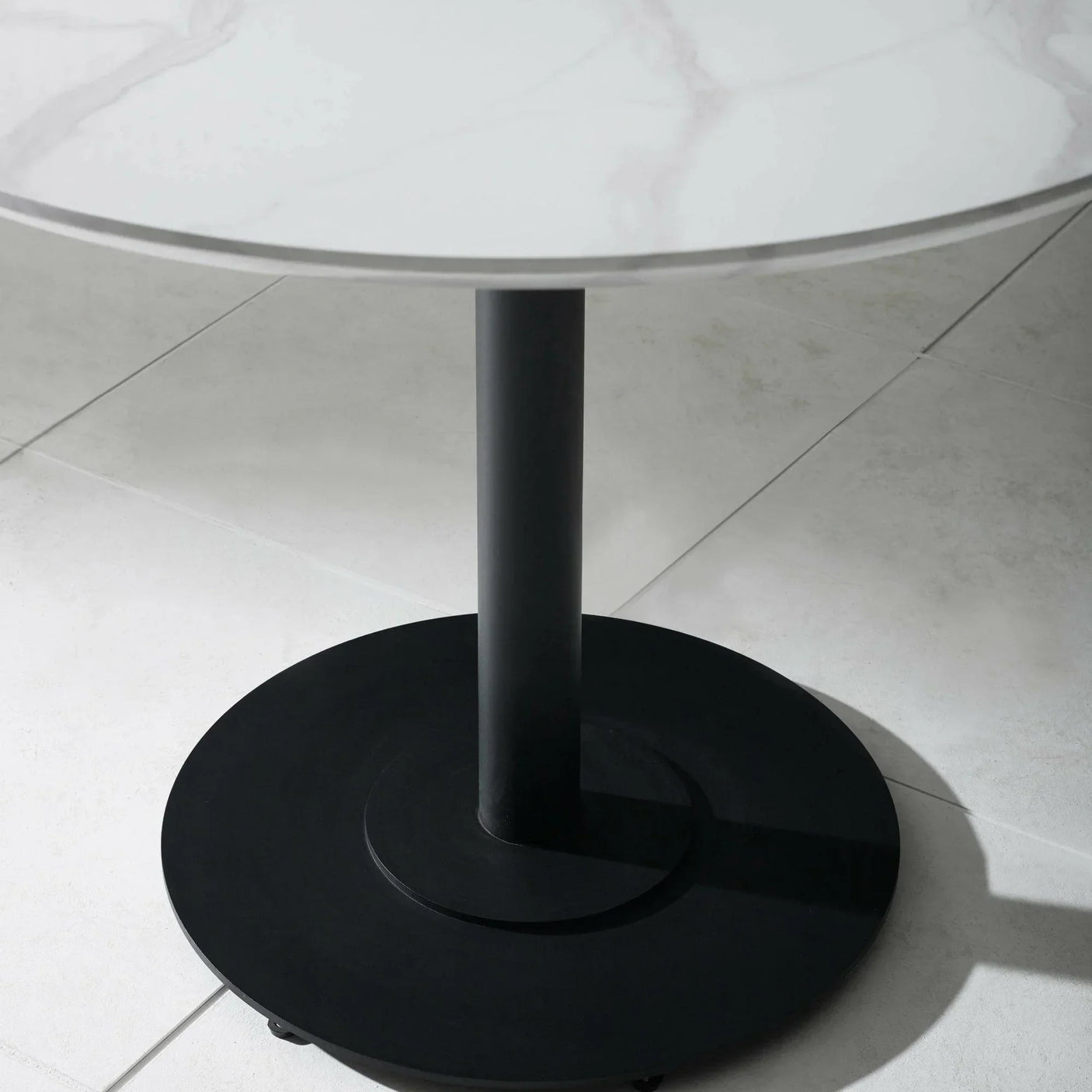 Round white marble dining table with black metal pedestal base on tiled floor