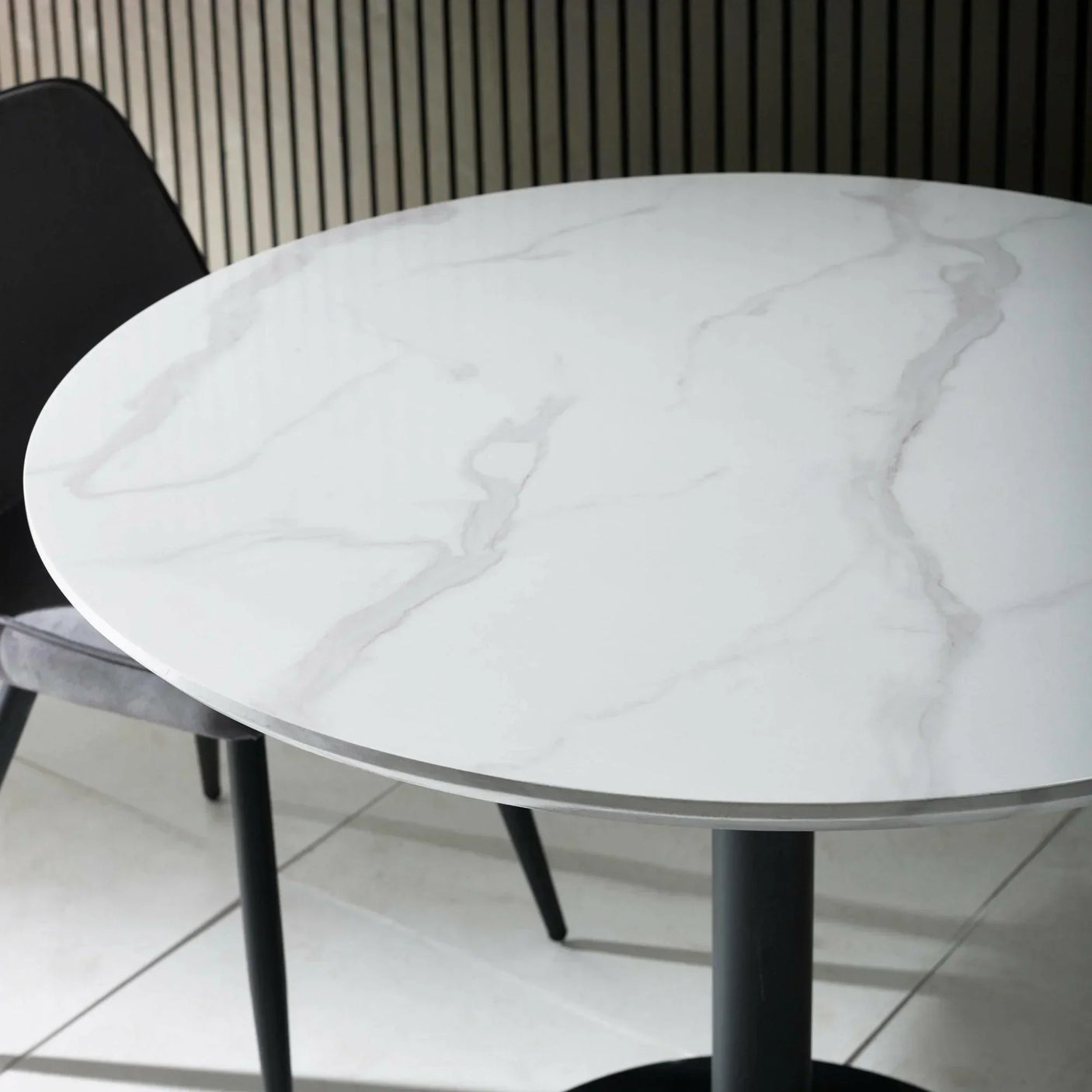 Round white marble dining table with black legs and grey chair on tiled floor