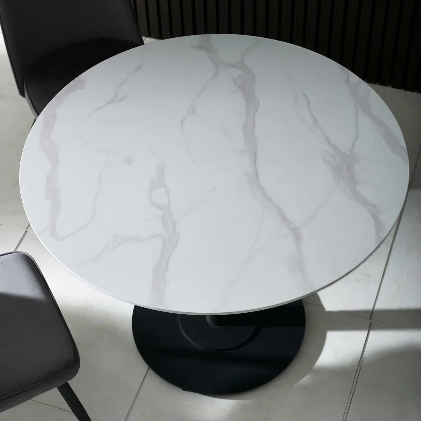 Round marble dining table with white veined top and black pedestal base, top view