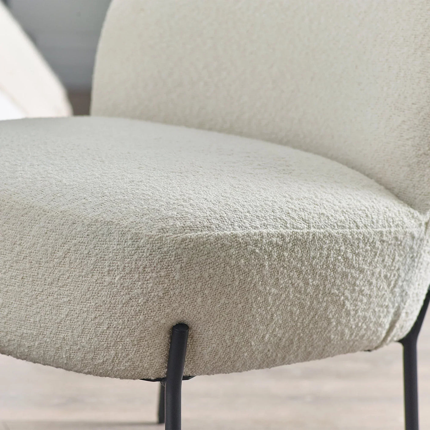Close detail of cream boucle accent chair seat with black metal legs on wooden floor