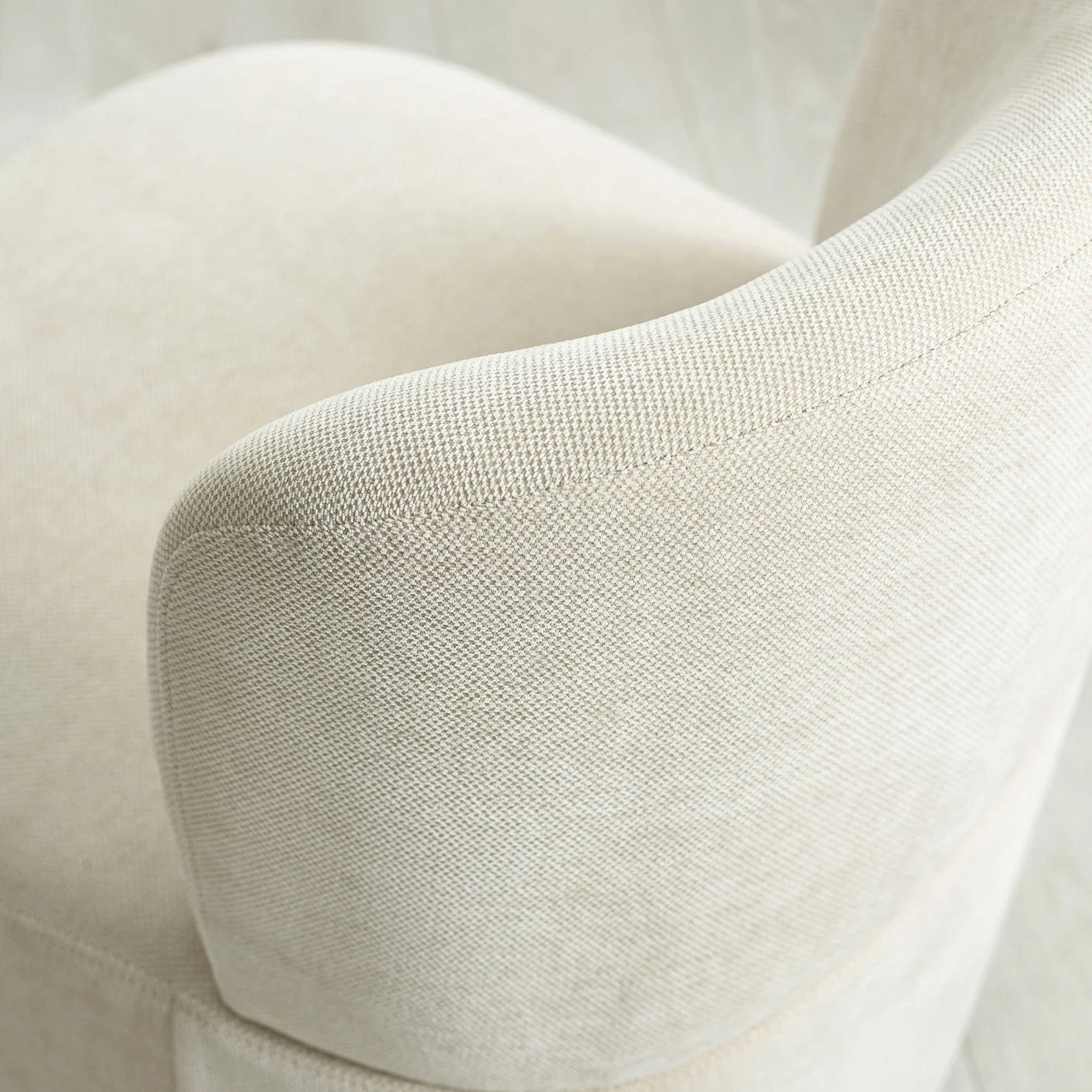 Curved beige fabric armchair with textured upholstery, close view of backrest and arm detail